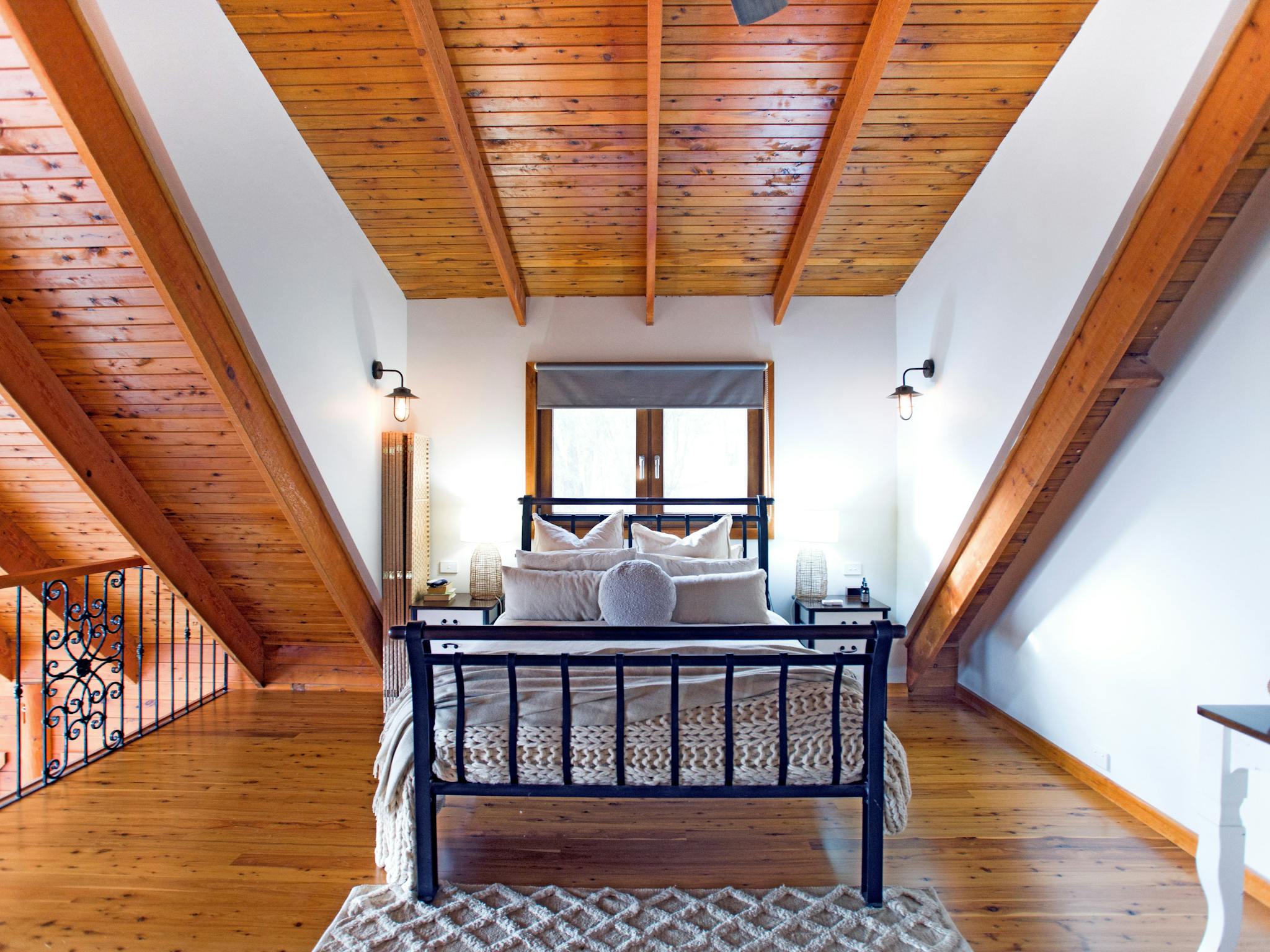 Loft bedroom with timber ceiling, iron bed, and warm lighting.