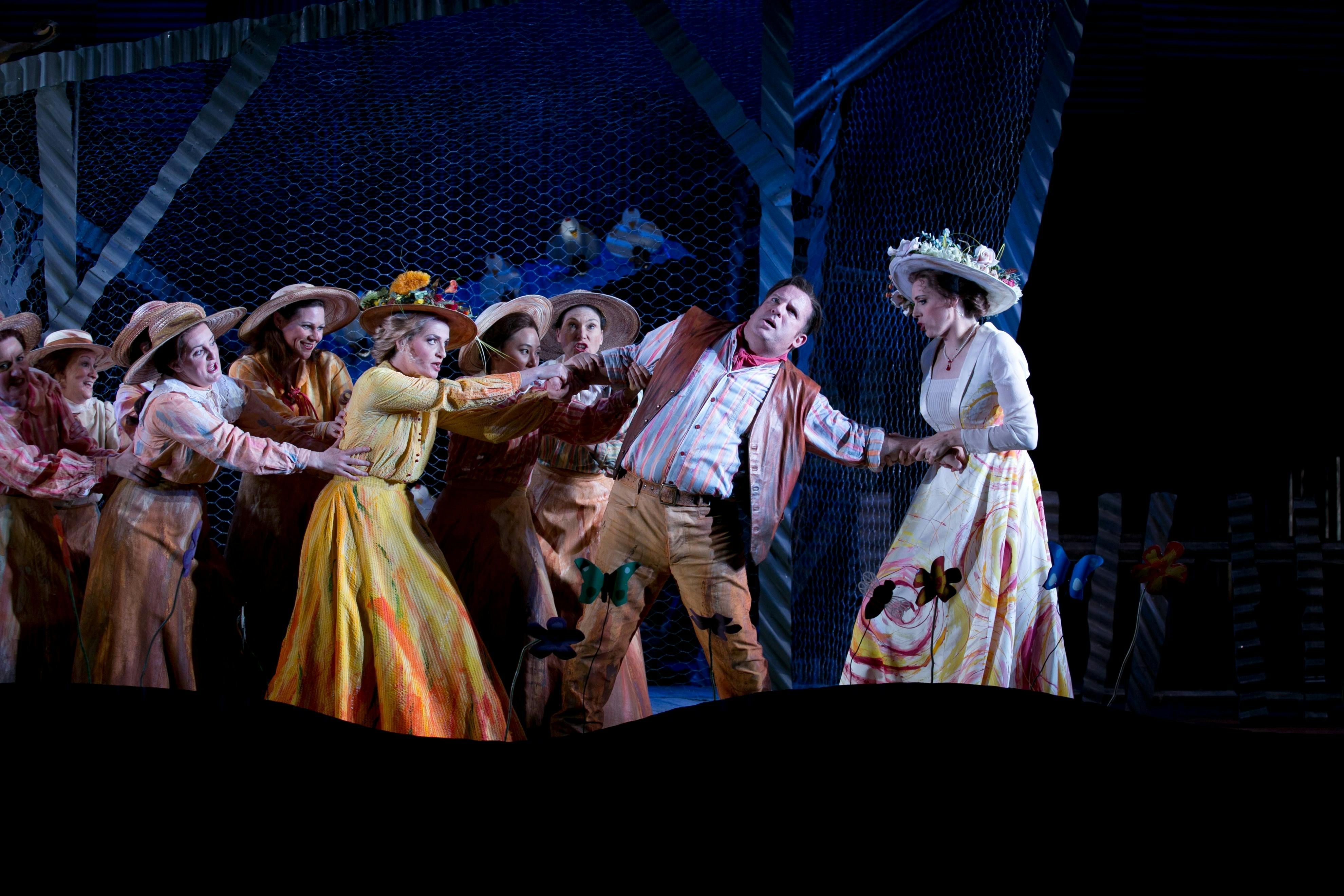 Ensemble cast on stage pull a performer between groups in a lively opera scene.