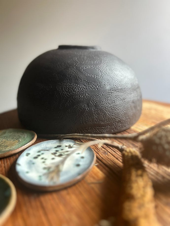 dark round ceramic vessel on a brown table with small blue and green plates