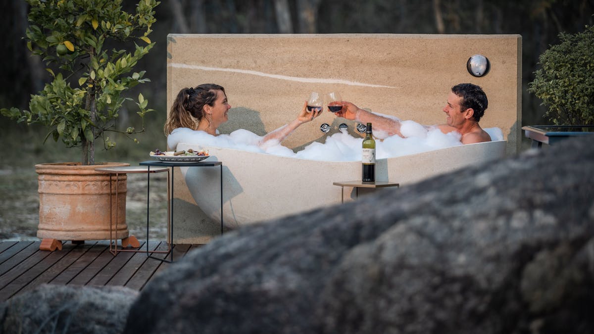 Luxury outdoor stone bath surrounded by rammed earth & granite amidst nature in Queensland Country