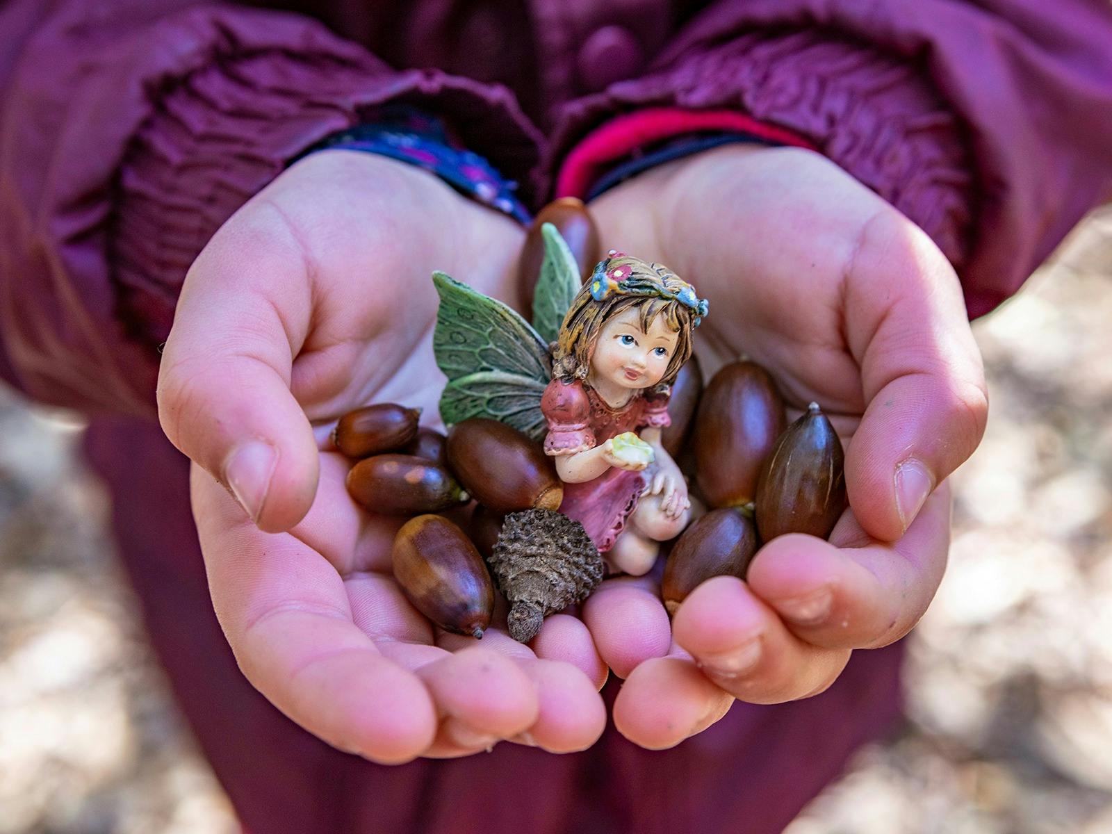 A child holds colourful seeds and a small purple fairy figurine