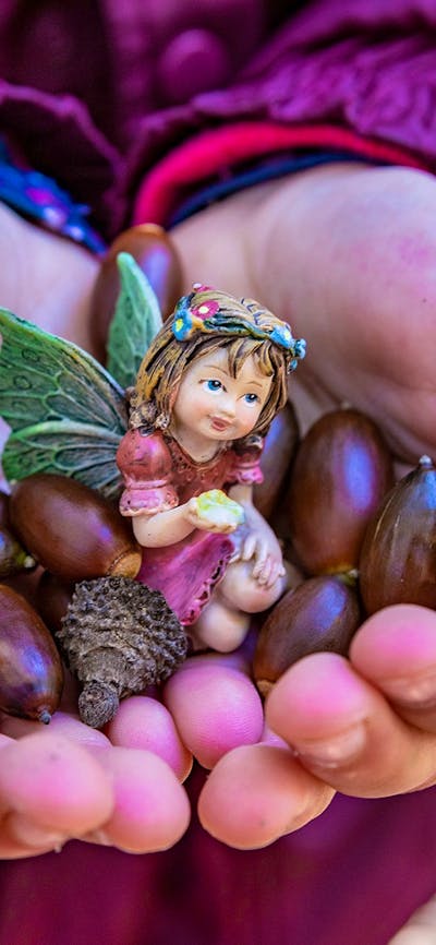 A child holds colourful seeds and a small purple fairy figurine