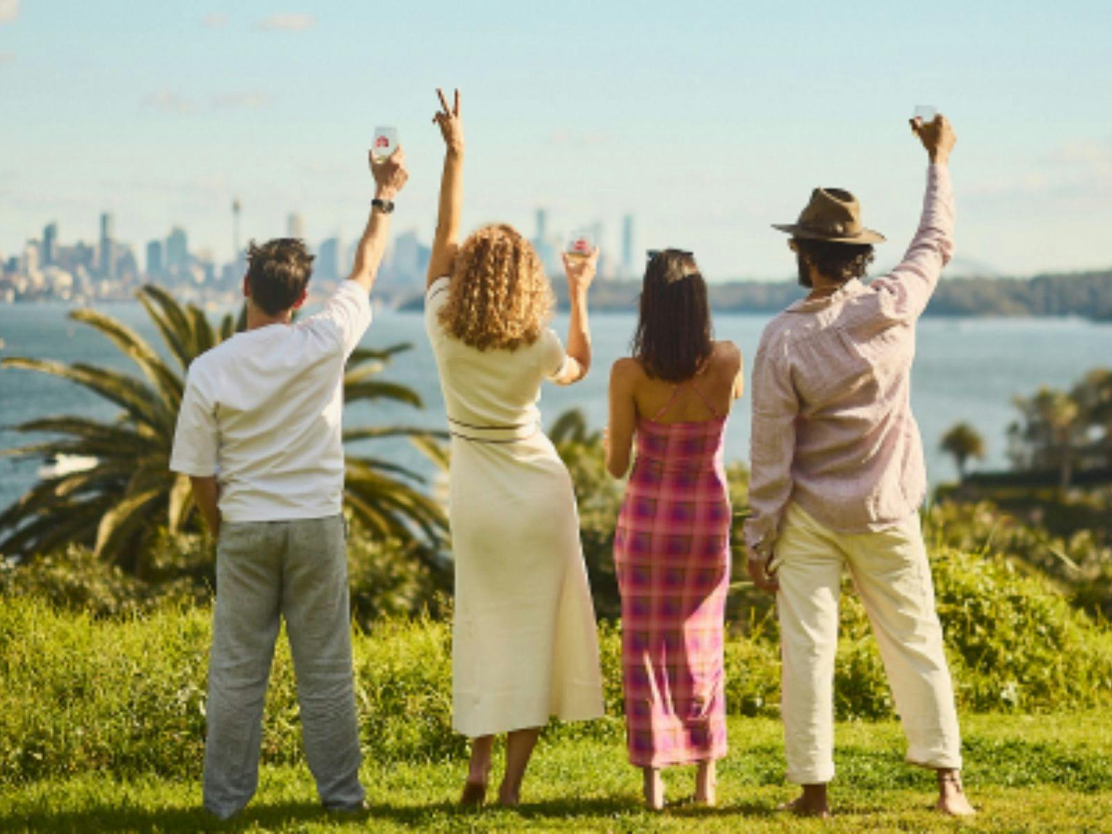 Two males and two females holding wine glasses facing the Sydney Harbour