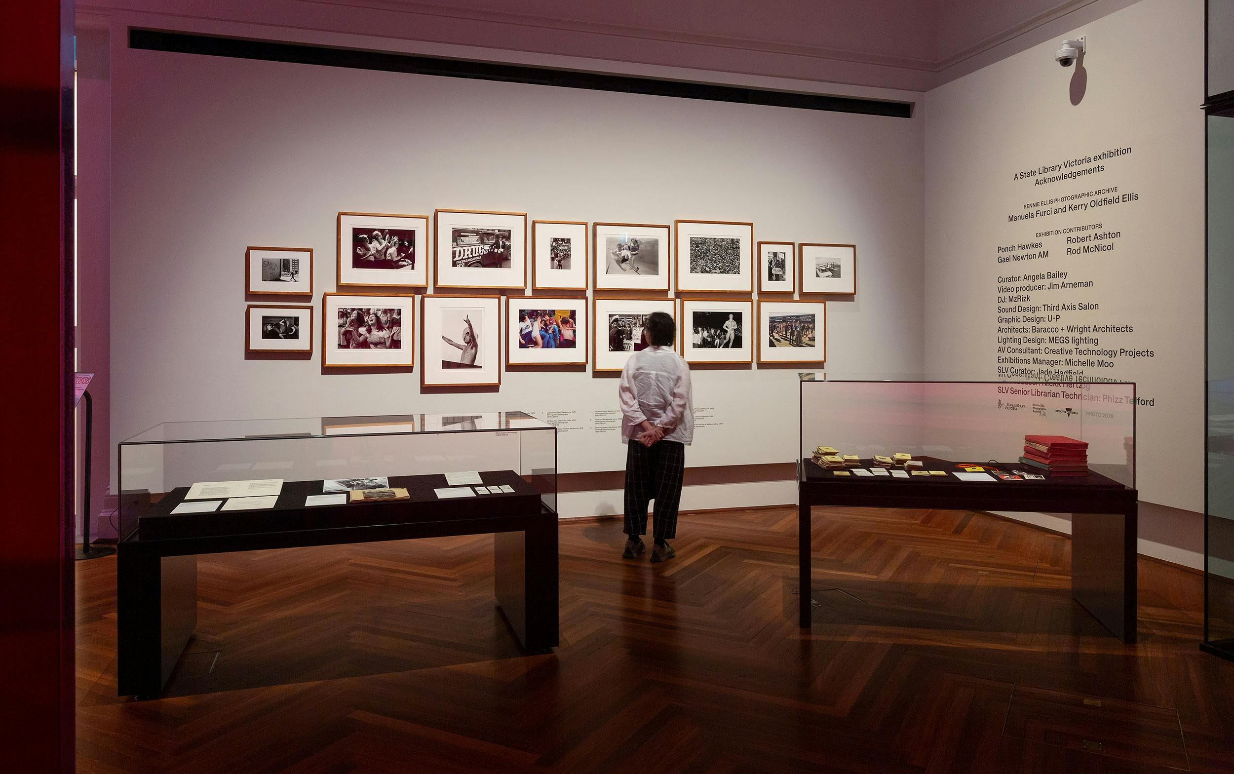 A white gallery wall full of photographs in frames, with a person  looking at them