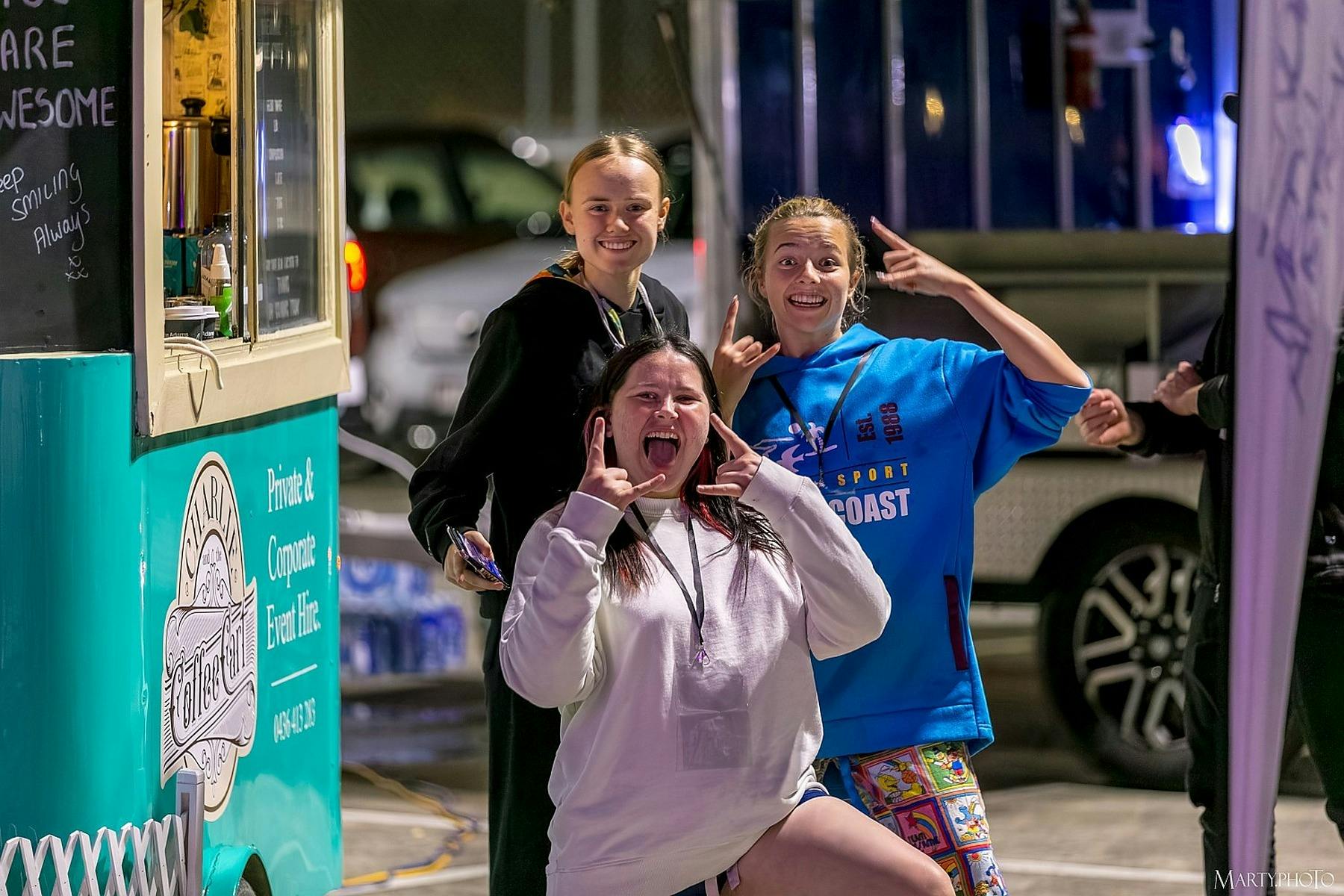 Three young participants smiling beside a food truck at the Gold Coast Live Like Her Challenge.