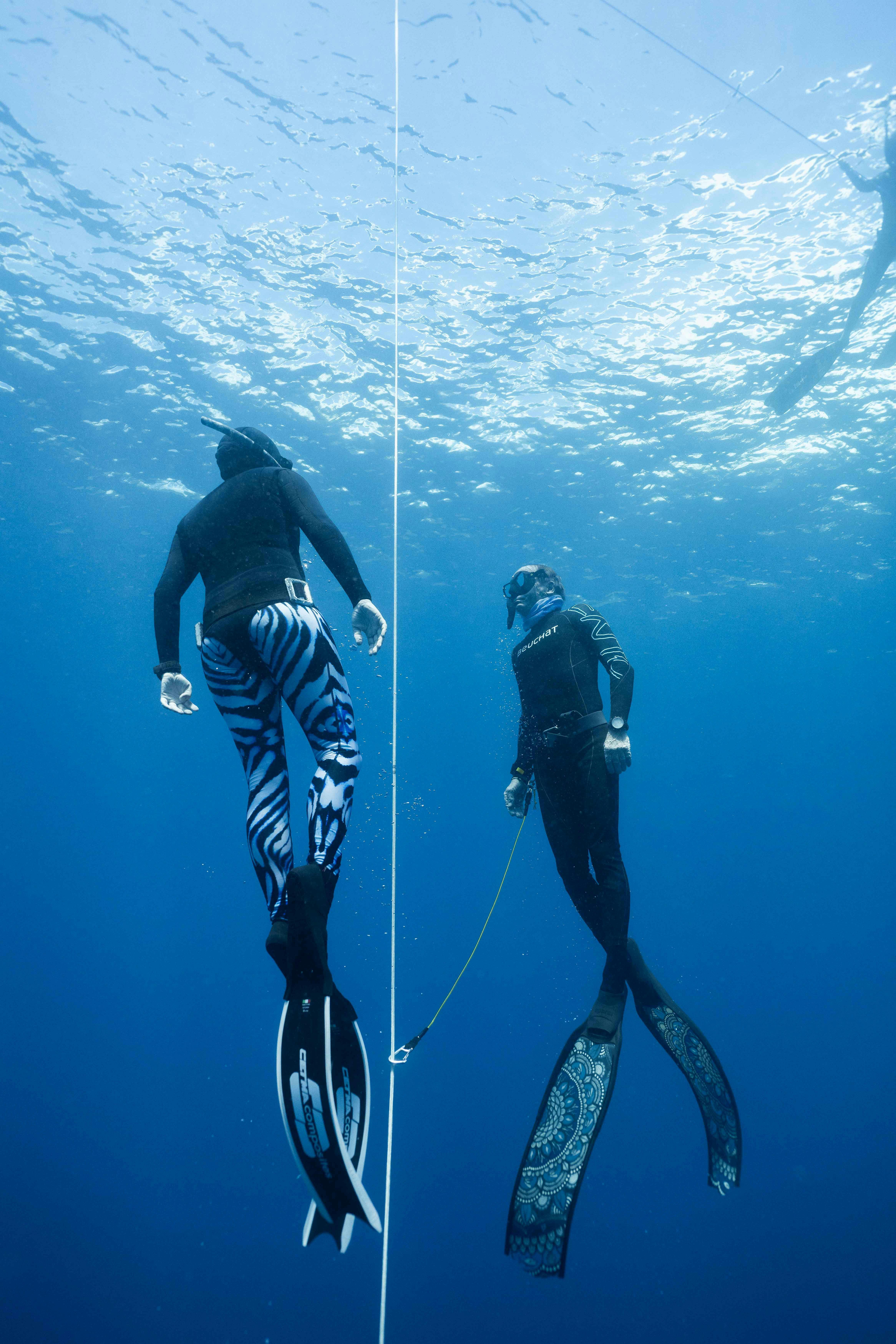 A freediver is diving up along the line with a instructor in front of him