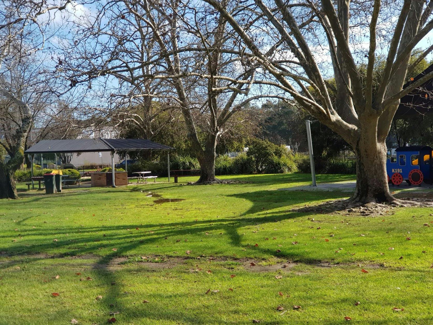 grass, trees, bbq, picnic tables, shelter, on right replica train in childrens playground