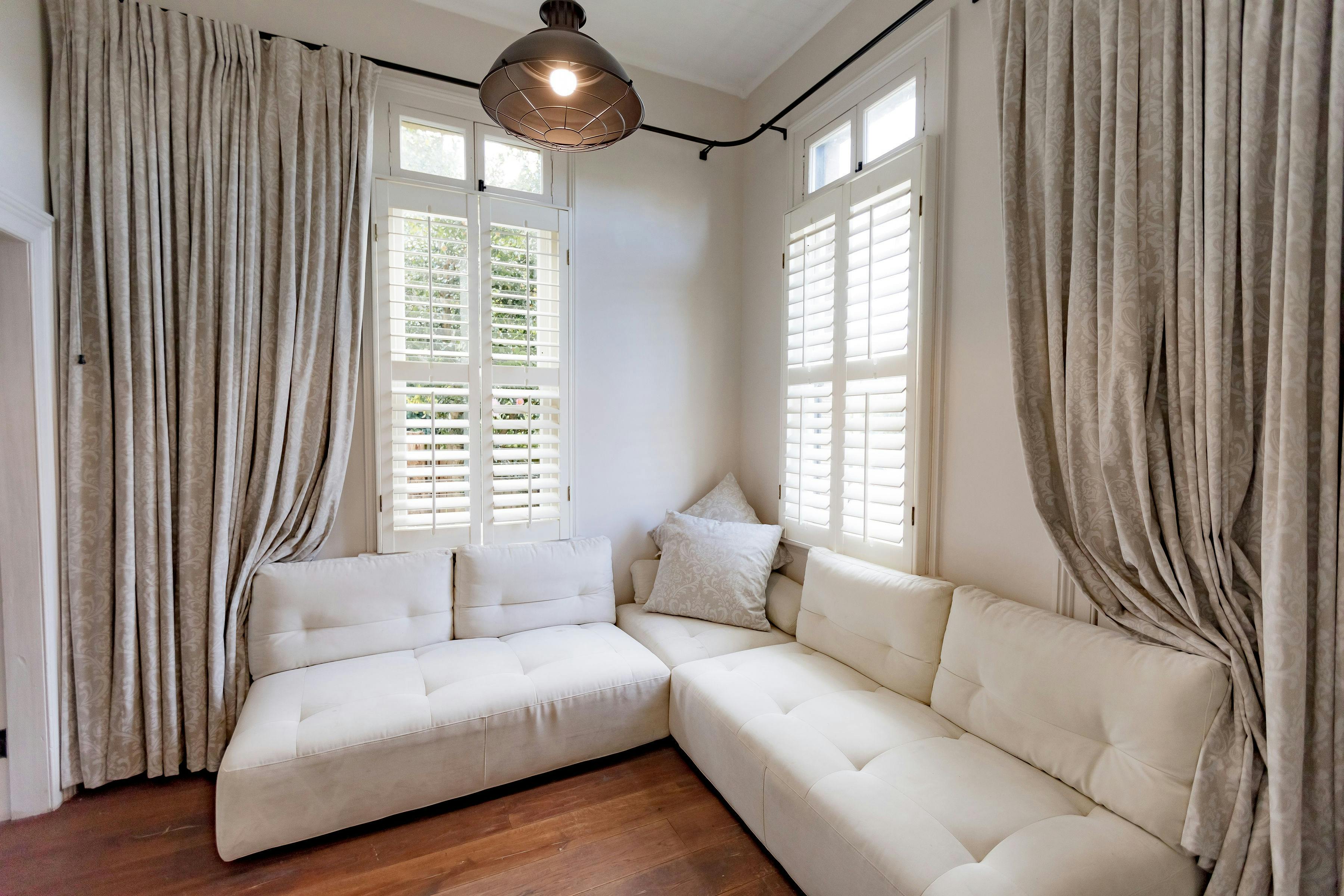 Corner configured cream couch surrounded by drapes and large windows