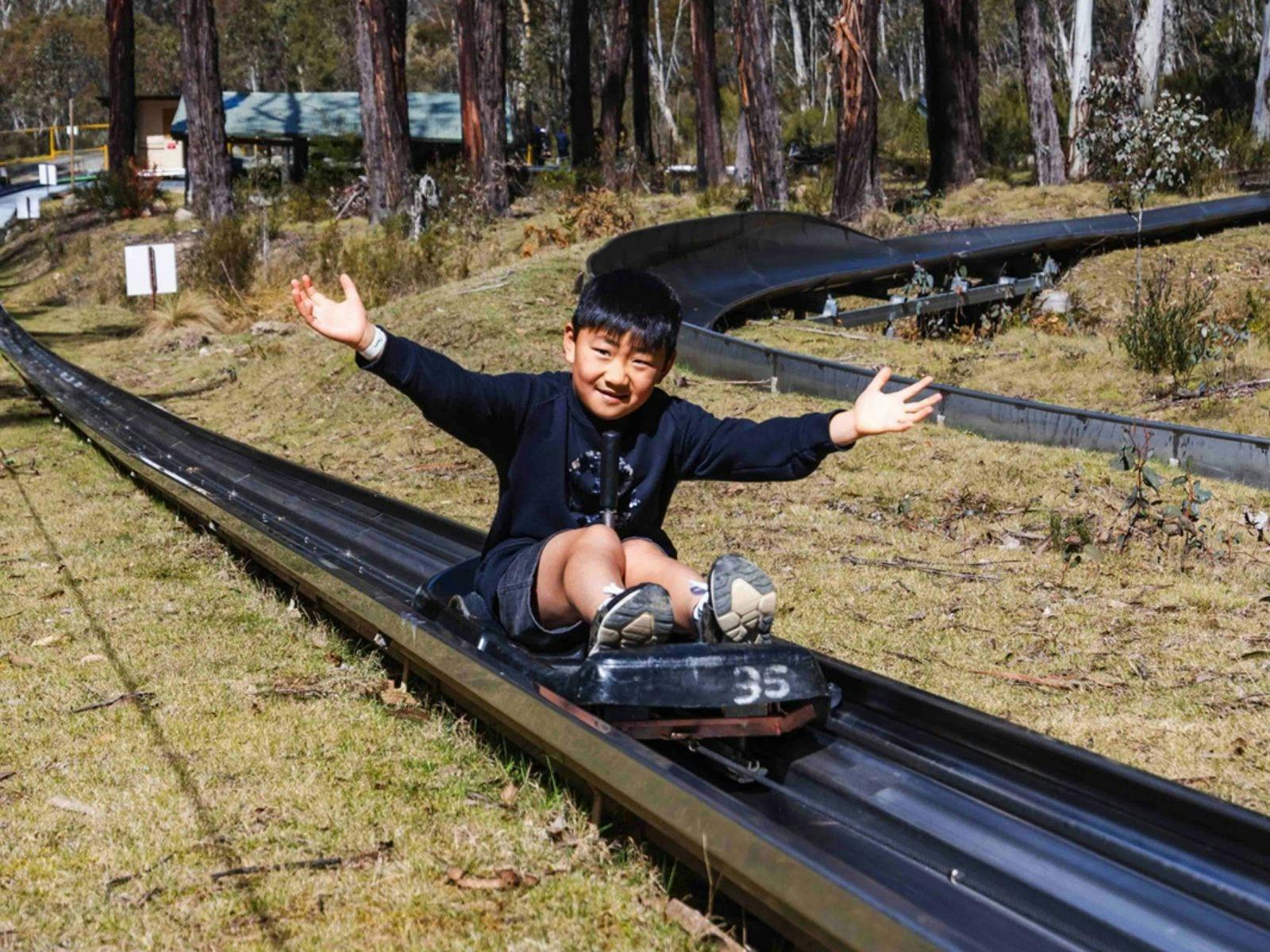 A smiling boy sits on a cart being towed uphill with his arms out to the side