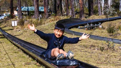 A smiling boy sits on a cart being towed uphill with his arms out to the side