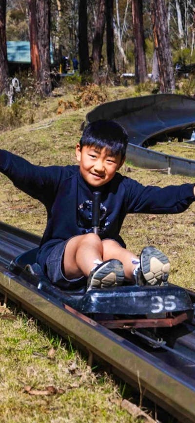 A smiling boy sits on a cart being towed uphill with his arms out to the side