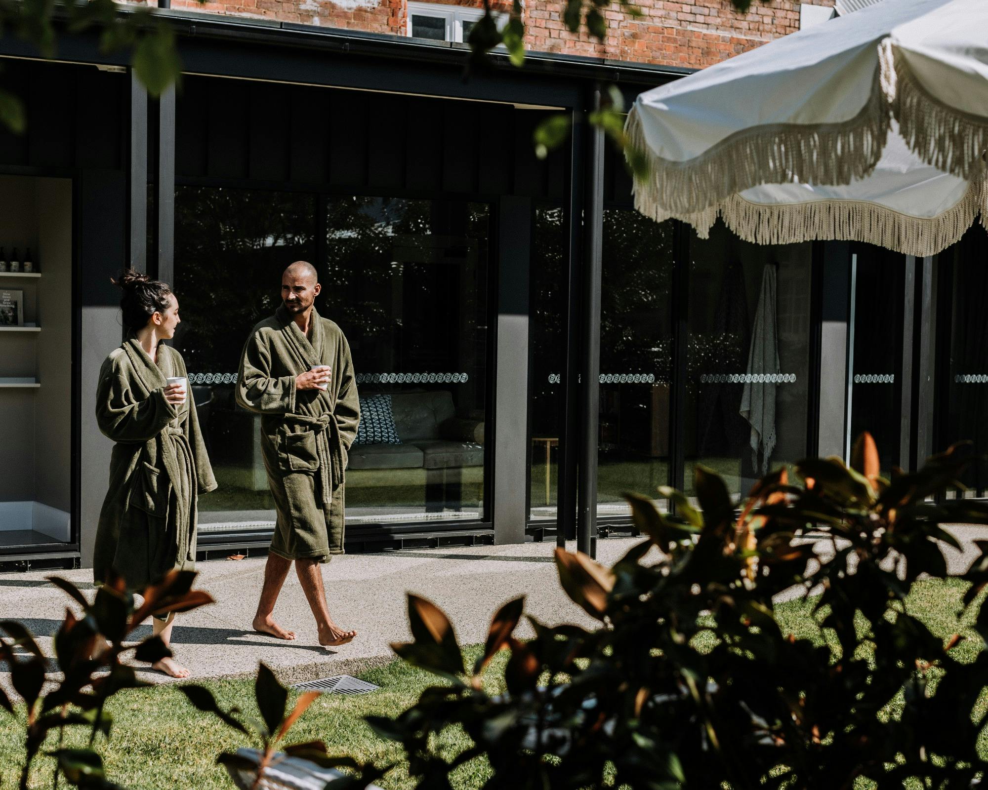 Couple walking outdoors in robes and with cup of hot beverage