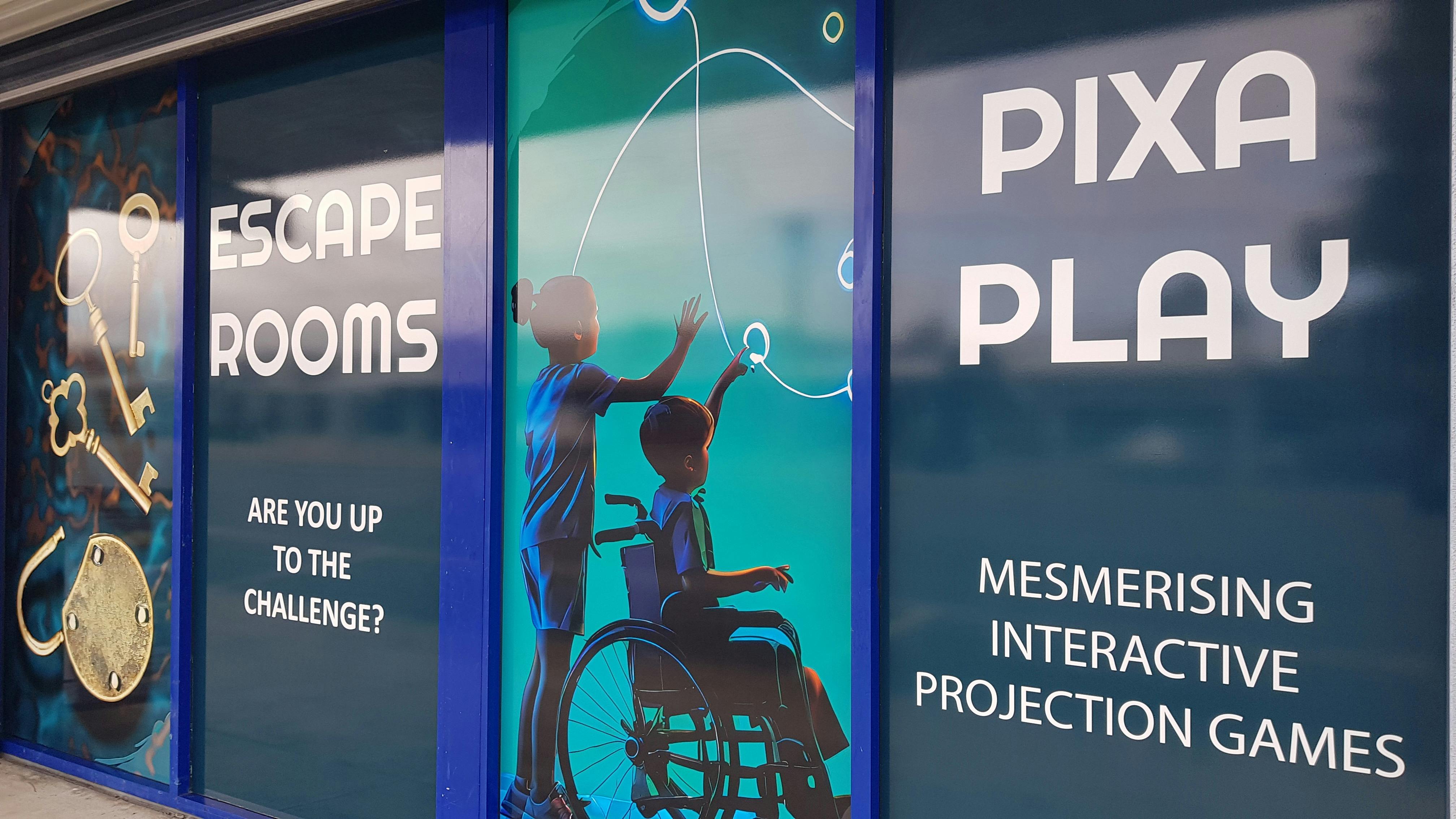 Single-level storefront with full-height signs showing people playing large-format digital games.