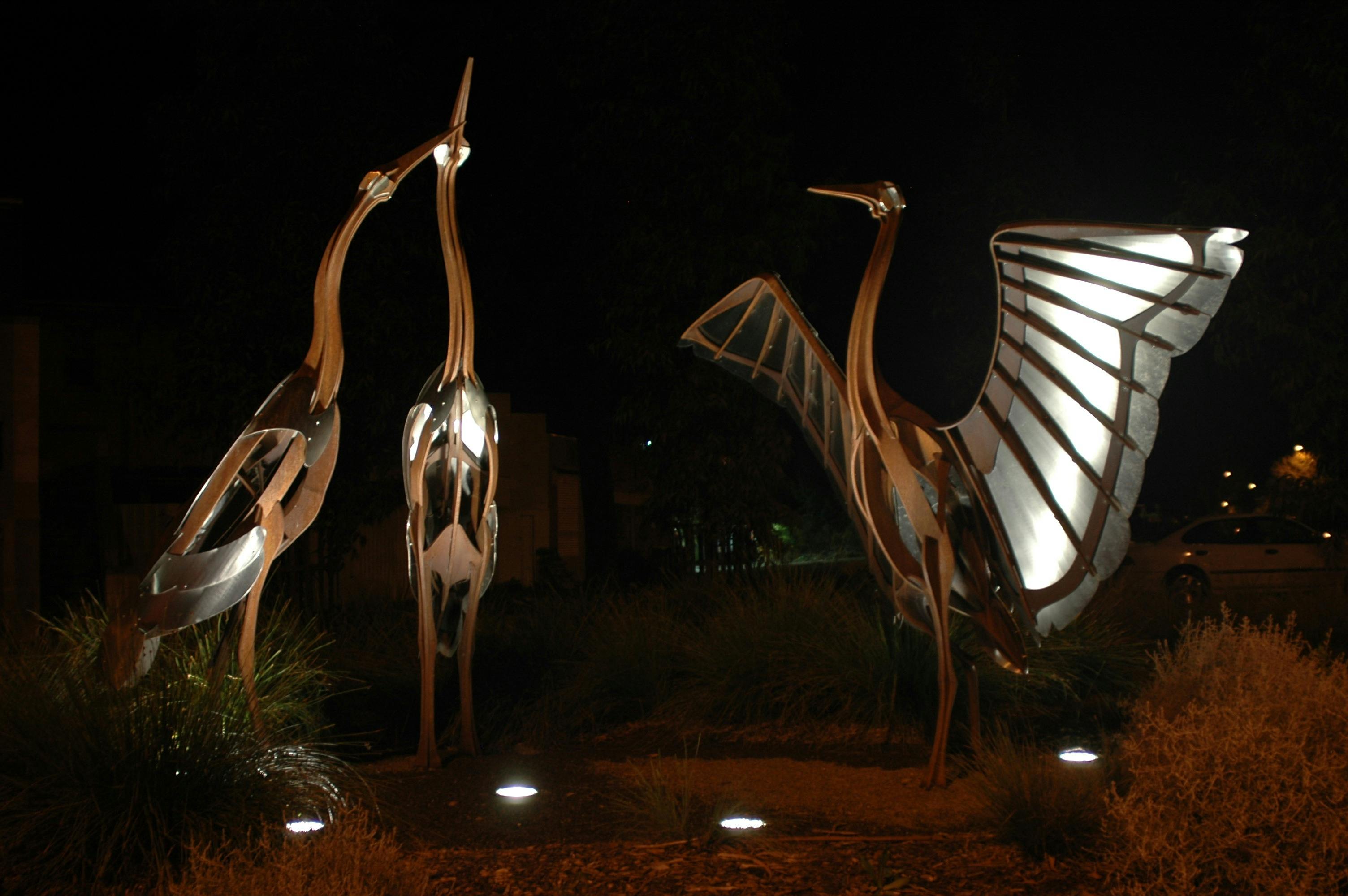 一個大型金屬雕塑，由三個布羅加斯組成，其中一個張開翅膀，拍攝於夜間。
