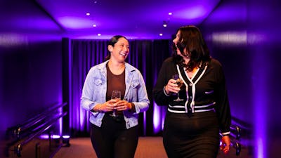 Two women walking down a hallway holding wine and laughing