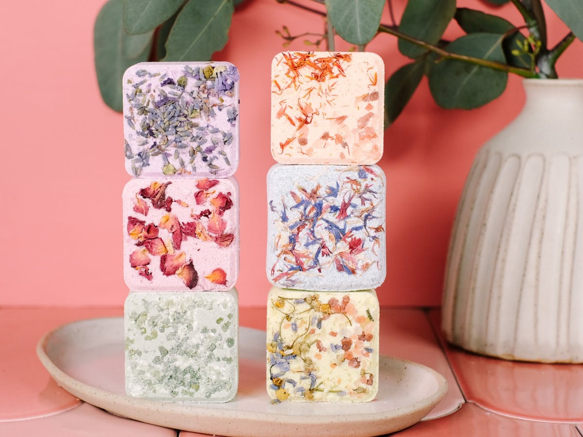 Image of 6 bath bombs, sitting on ceramic plate, next to vase with native plant.