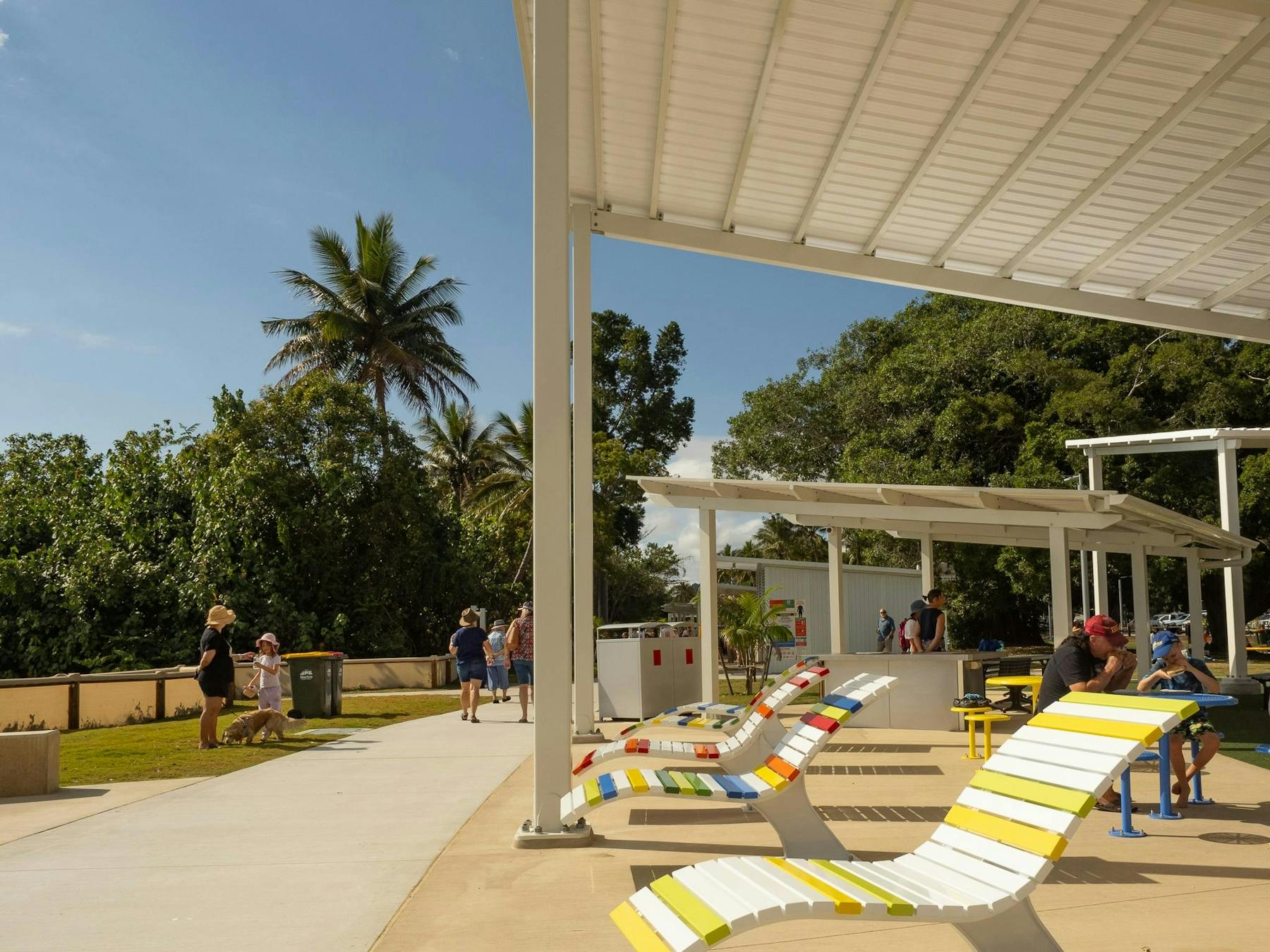 Sunchairs facing teh beach, tables and bbqs for family to cook, footpath with people walking dogs.