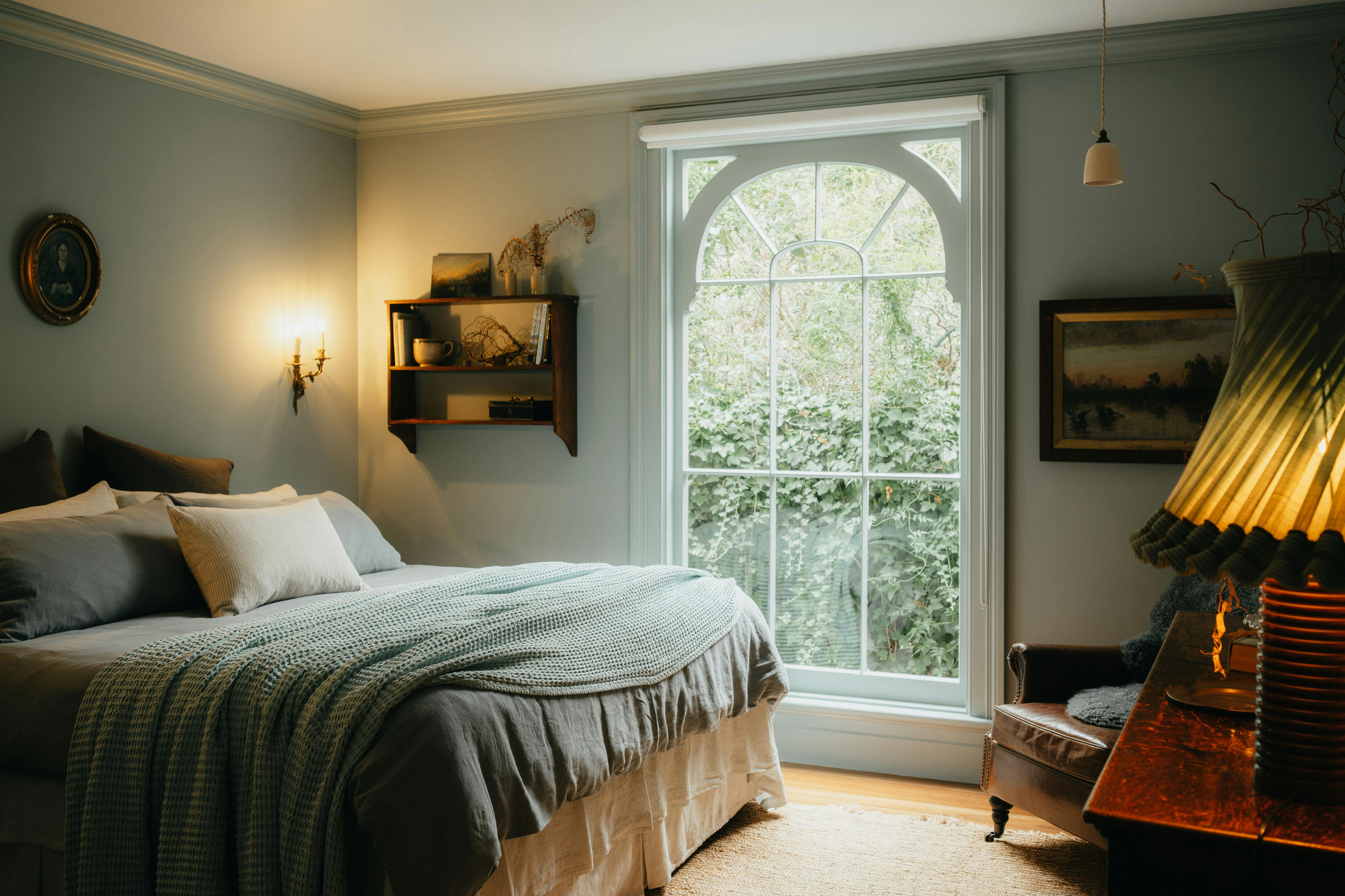 Bedroom with large arched window, double bed, soft linens and garden view.