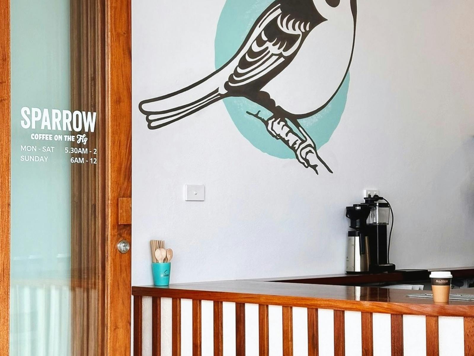 Photo looking into cafe with sparrow bird mural on wall. Nice timber benchtop with coffee machine