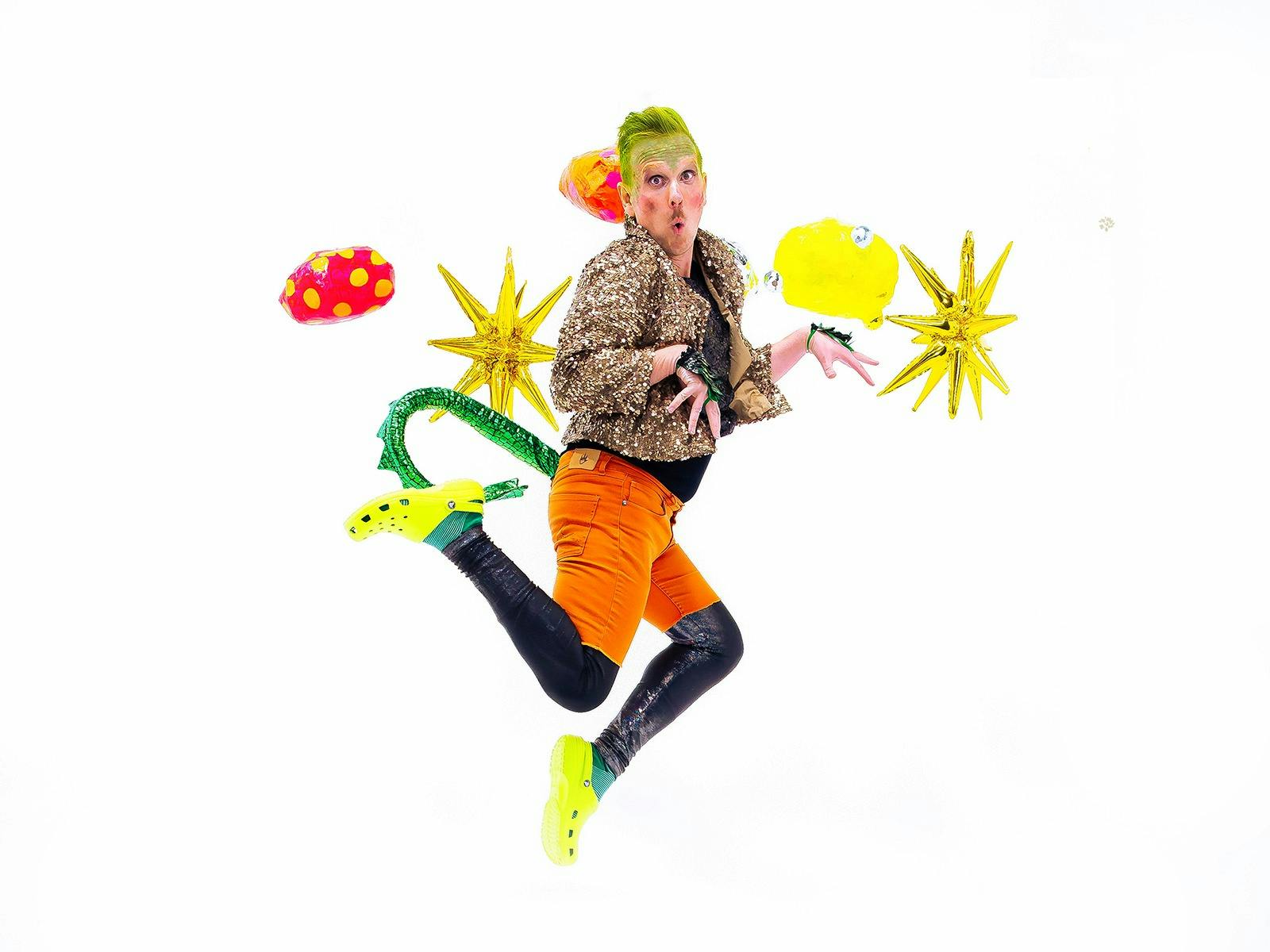 A man wearing a dinosaur tail is prancing through the air. Inflatable gold stars behind him.