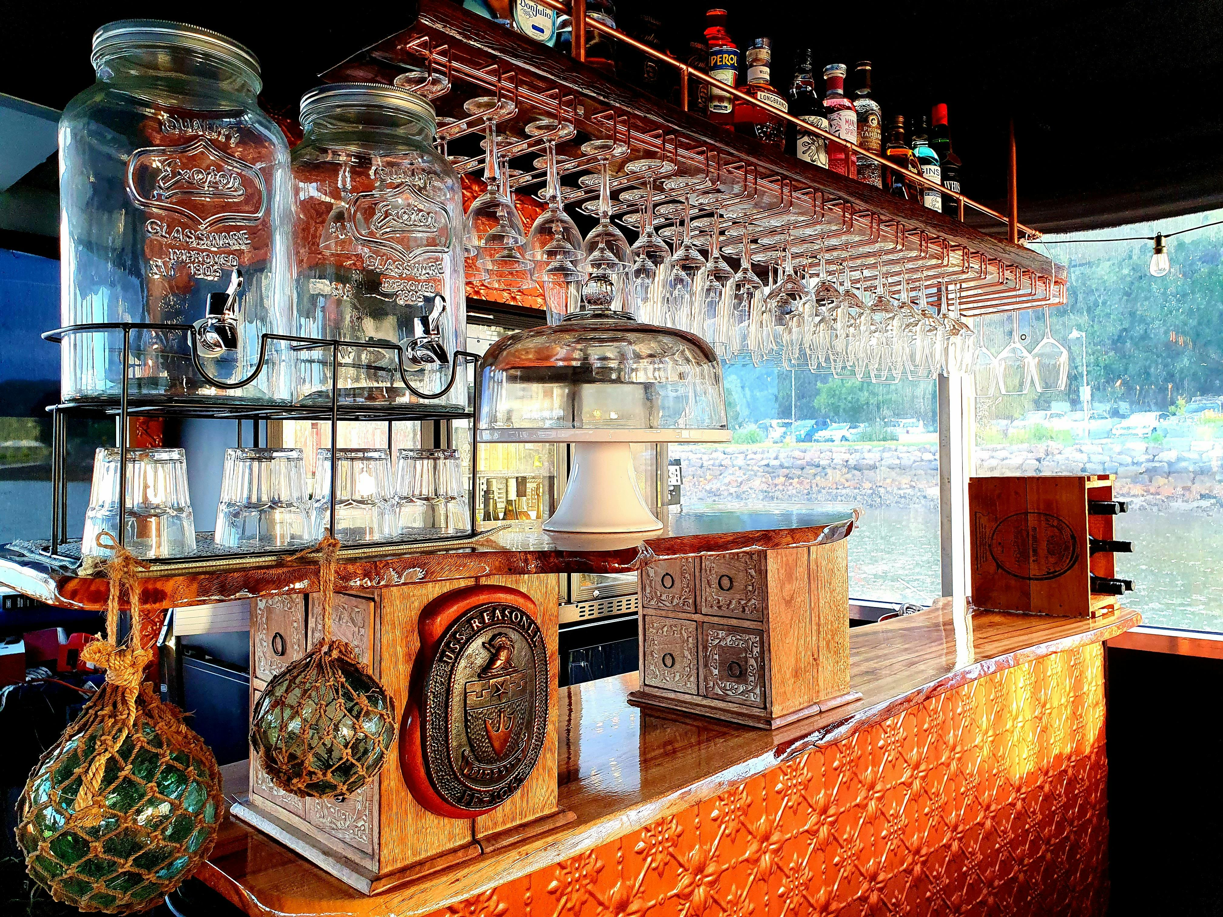 Bar at The Floating Oyster. Glass fishing floats & copper bar. Hanging wine glasses & sprits above.