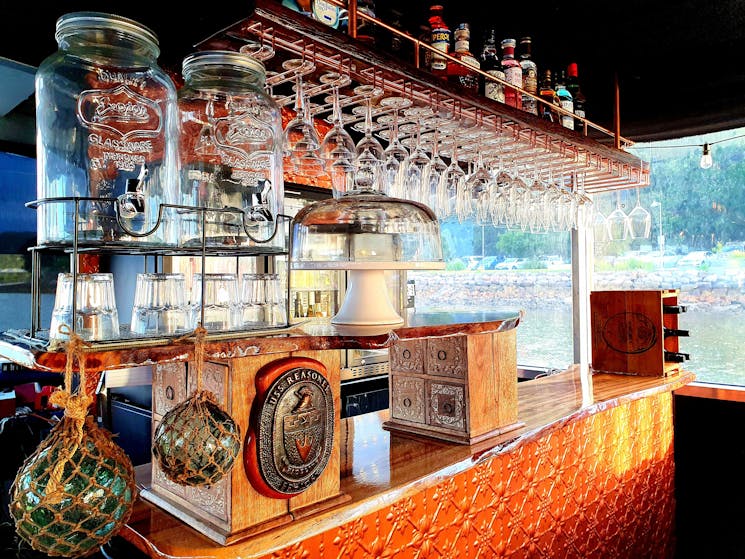 Bar at The Floating Oyster. Glass fishing floats & copper bar. Hanging wine glasses & sprits above.