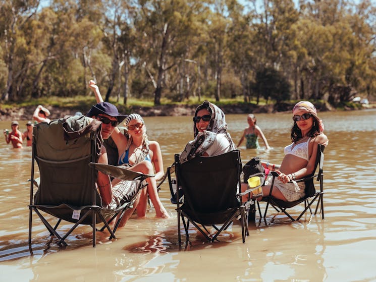 Two young men and two young women sit with camping chairs in the River Murray smiling