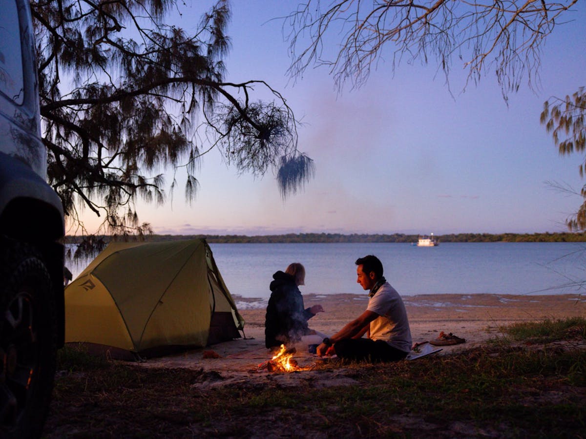 A couple looking out at the water as the sunsets with a fire