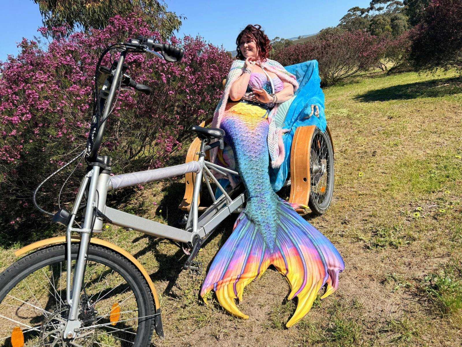 A woman wearing a mermaid costume, lounging on the back of an e-TukTuk in McLaren Vale