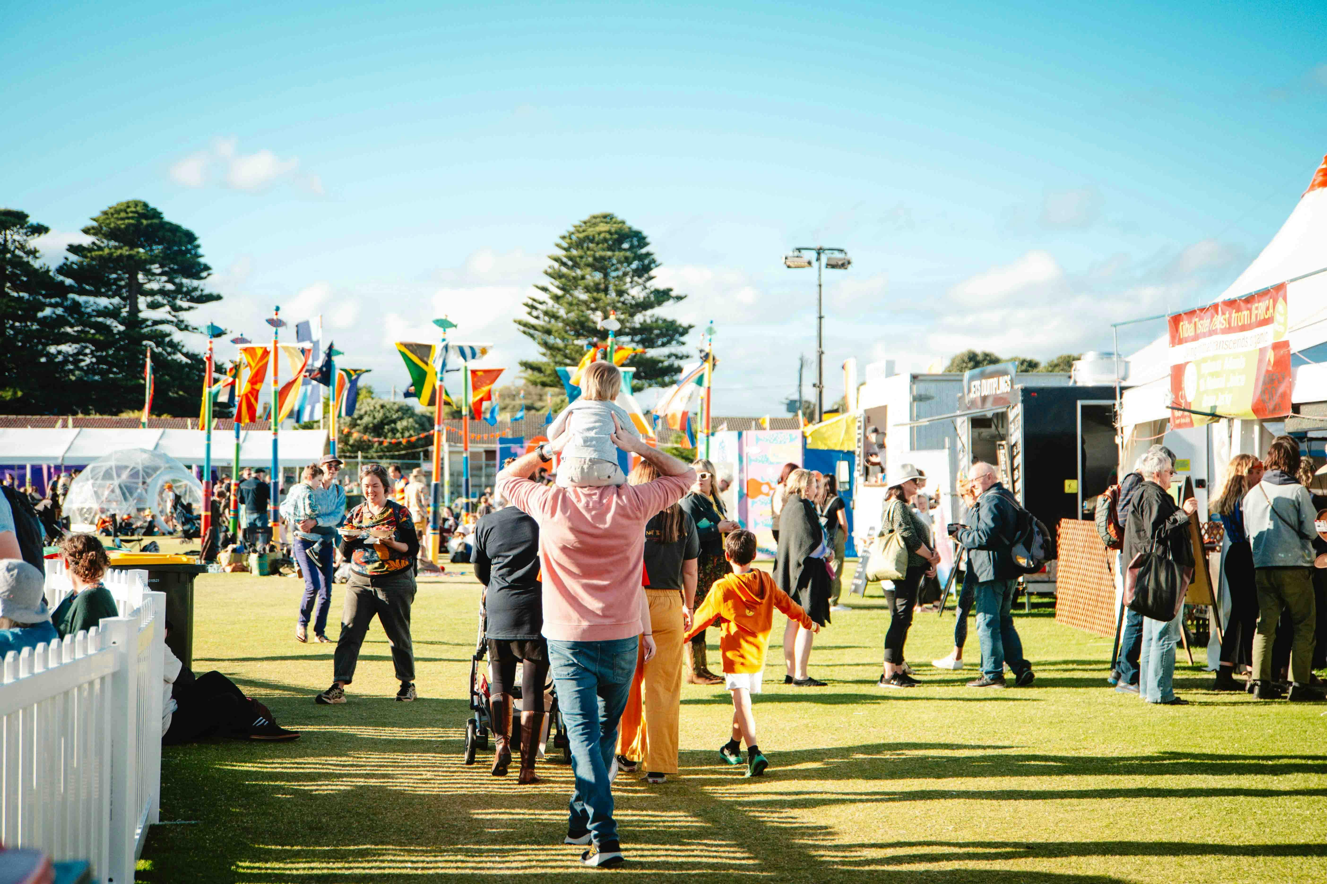 A child on shoulders of an adult at Port Fairy Folk Festival. The sky is very blue.