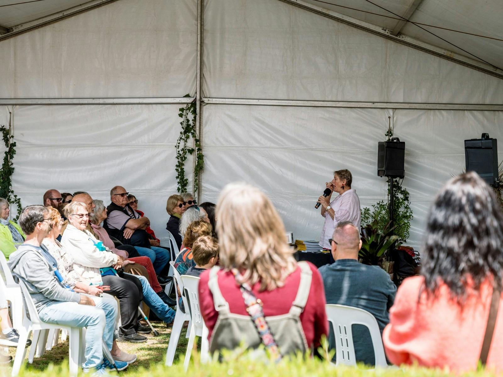 Wide image of a guest speaker in a marquee presenting to a group of patrons