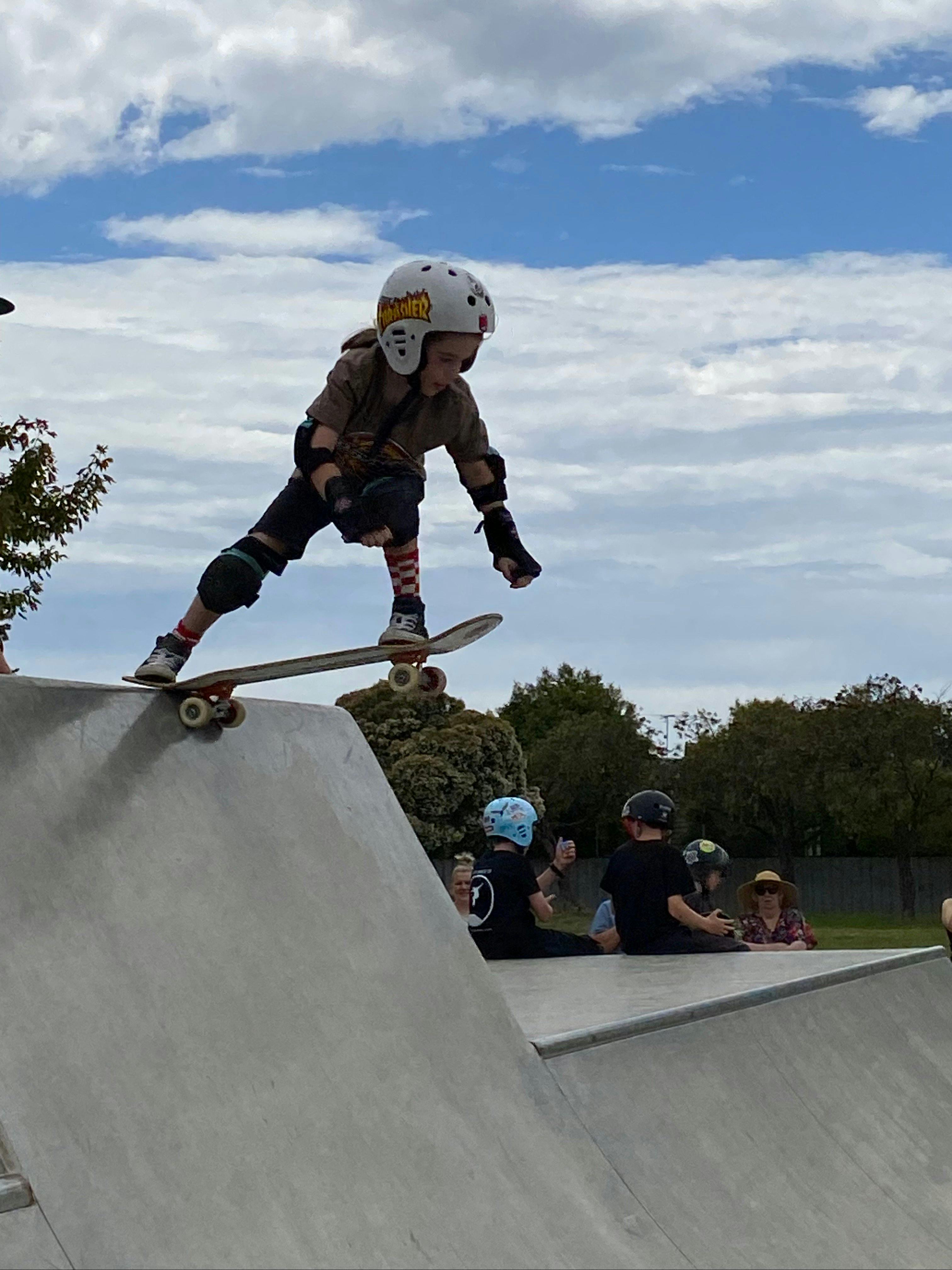 Child on top of cement skate park doing a trick in the air with other people watching in background