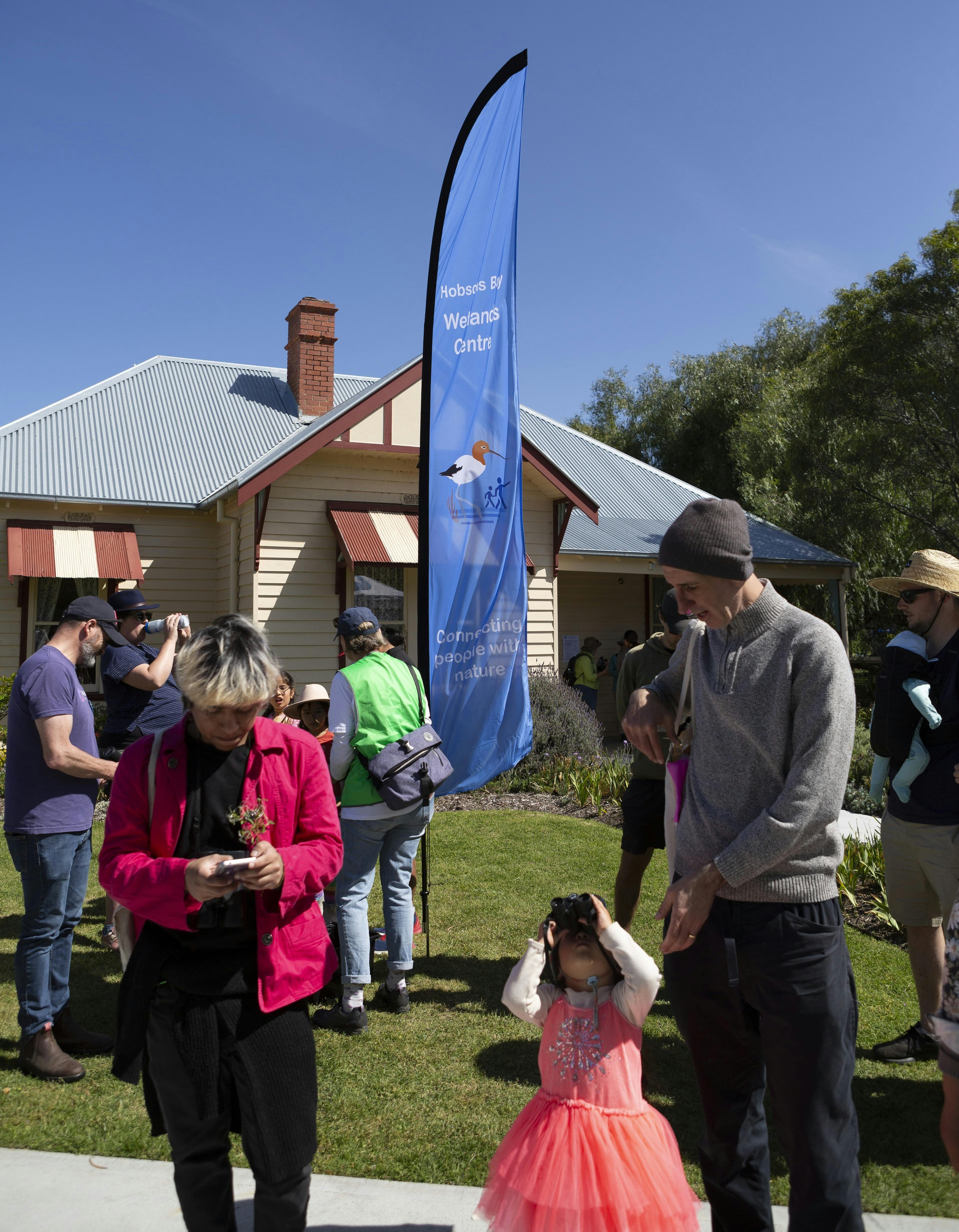 People waiting to go on a bird walk in front of a house and flag.