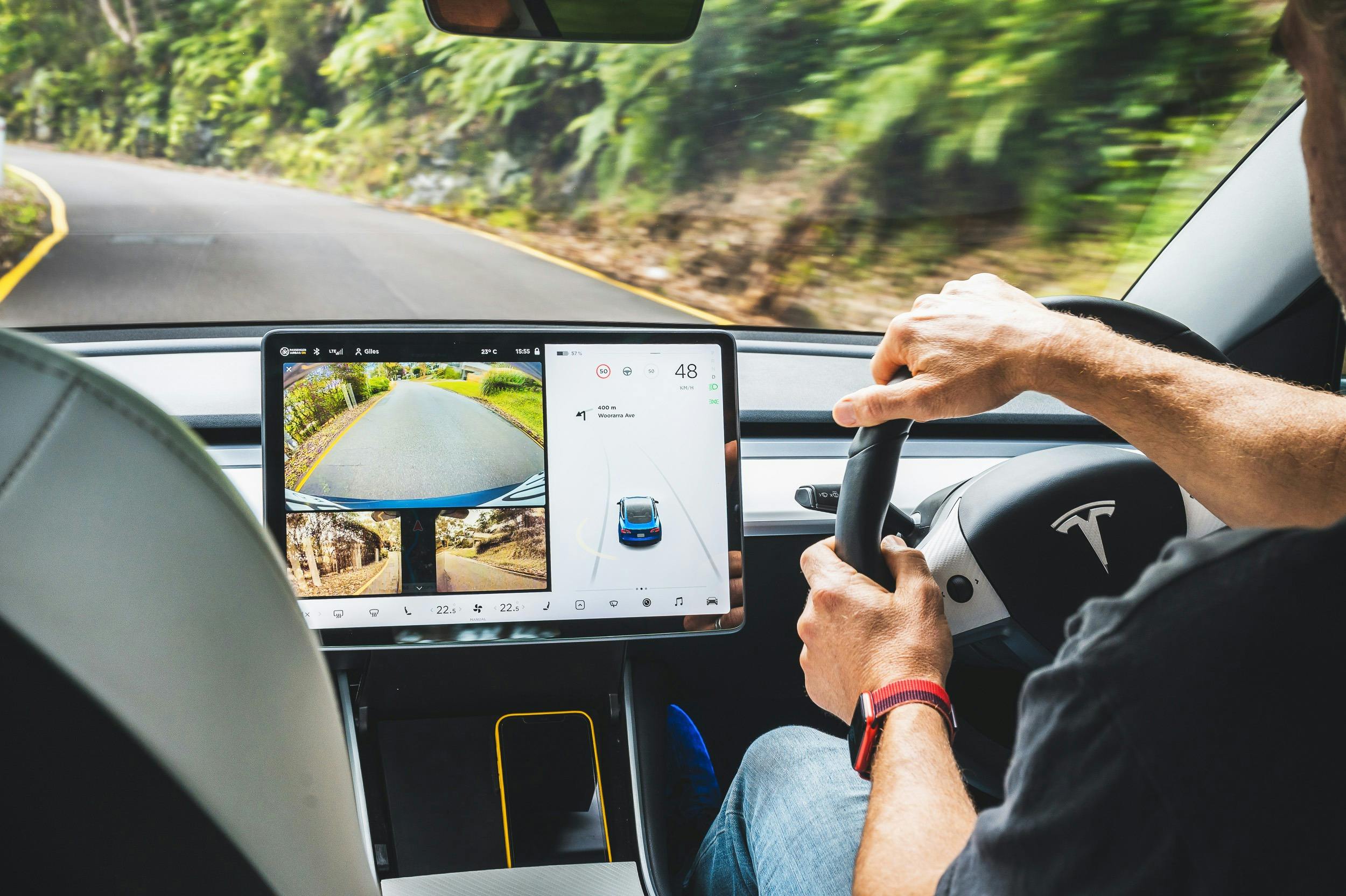 view from inside car of man driving tesla and screen on showing reverse camera image