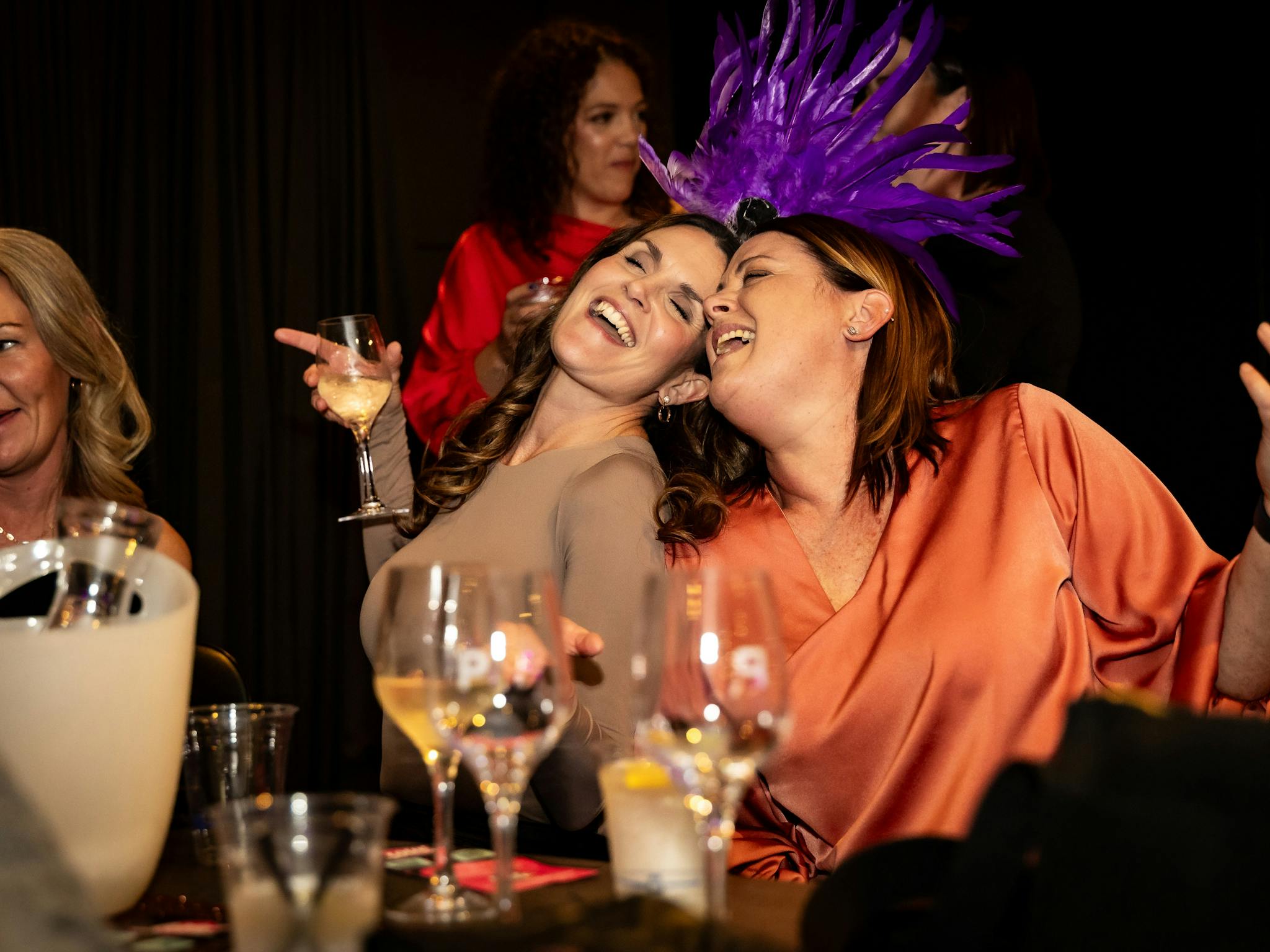 Two ladies sitting with heads together are singing happily holding glasses of wine Two ladies sitting with heads together are singing happily holding glasses of wine