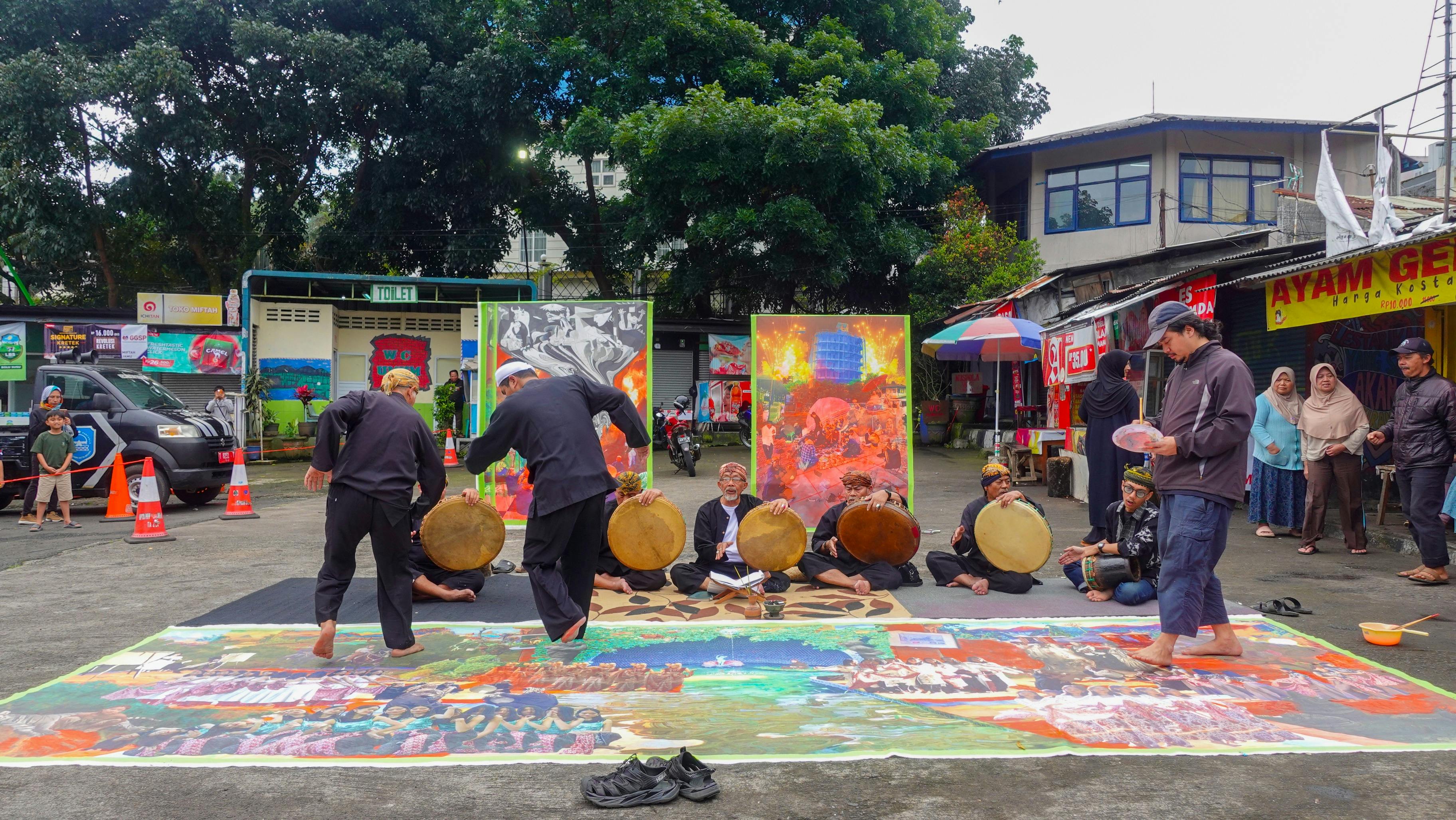 Work in progress of artwork outside on the ground with outdoor stalls and musicians seated