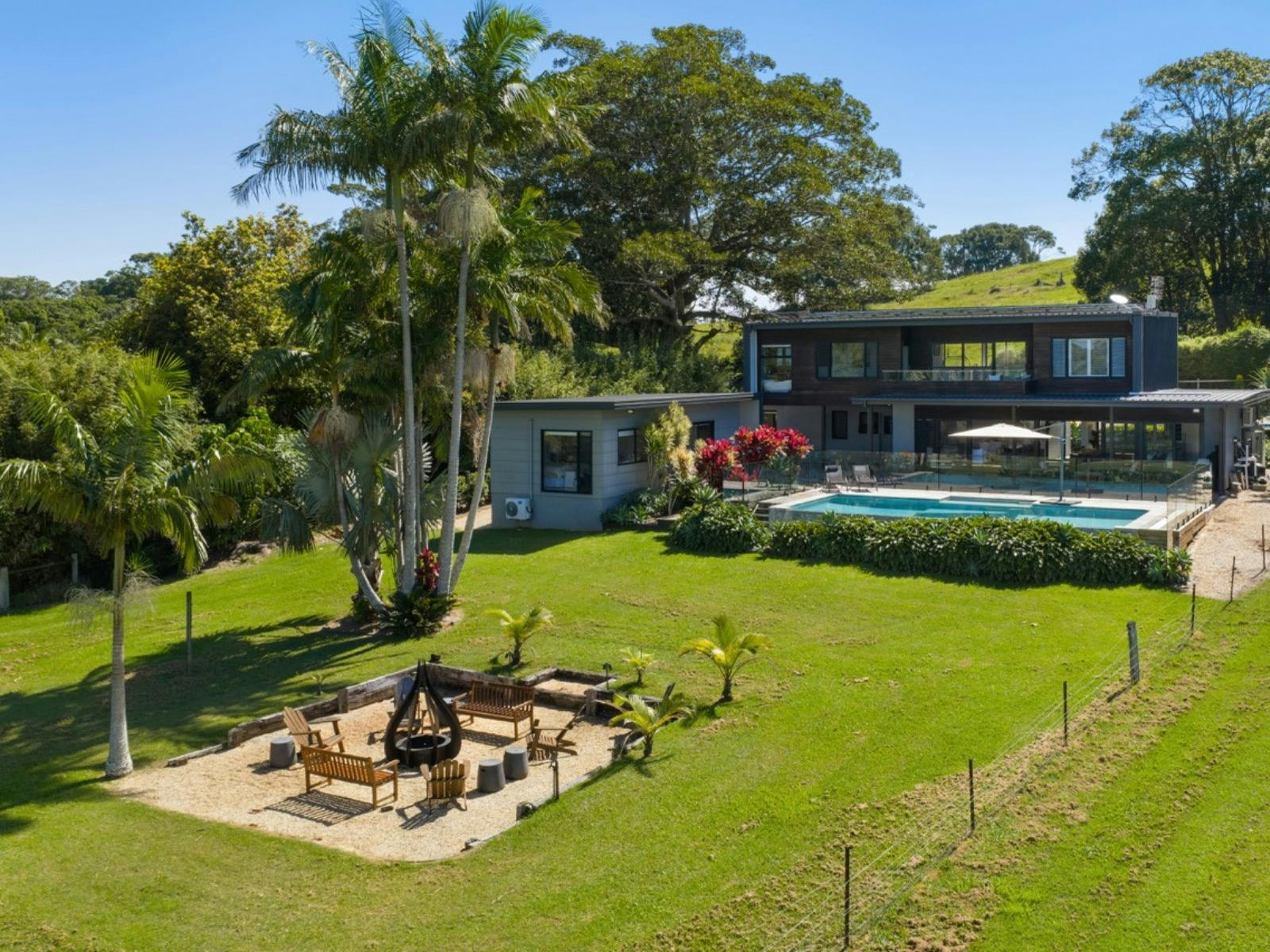 Aerial view of luxury home with pool, fire pit, tropical gardens and expansive lawns.