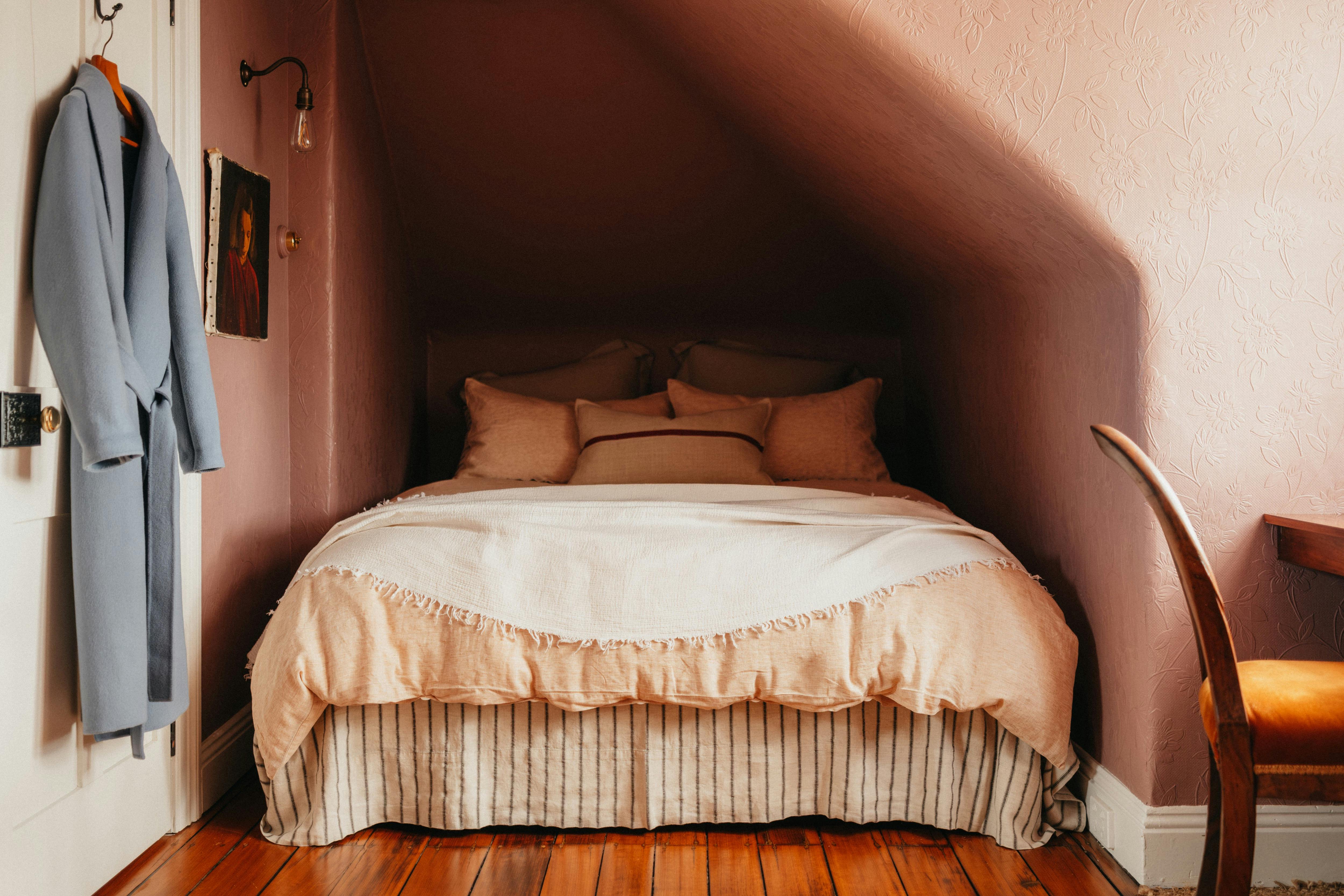 Small bedroom with double bed, pink walls, timber floor and soft bedding.