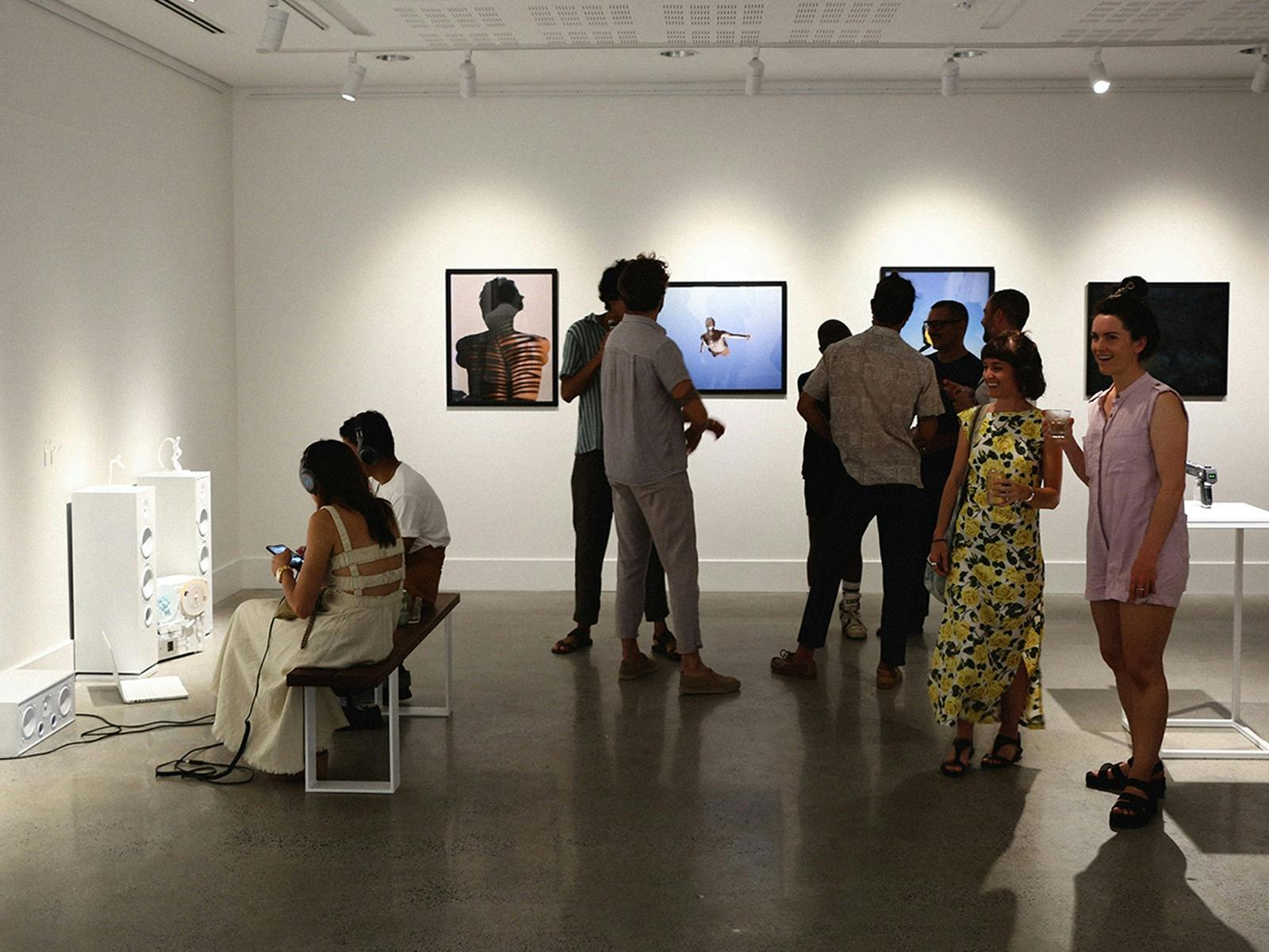 People are standing in the gallery listening to sound art on headphones and looking at photographs