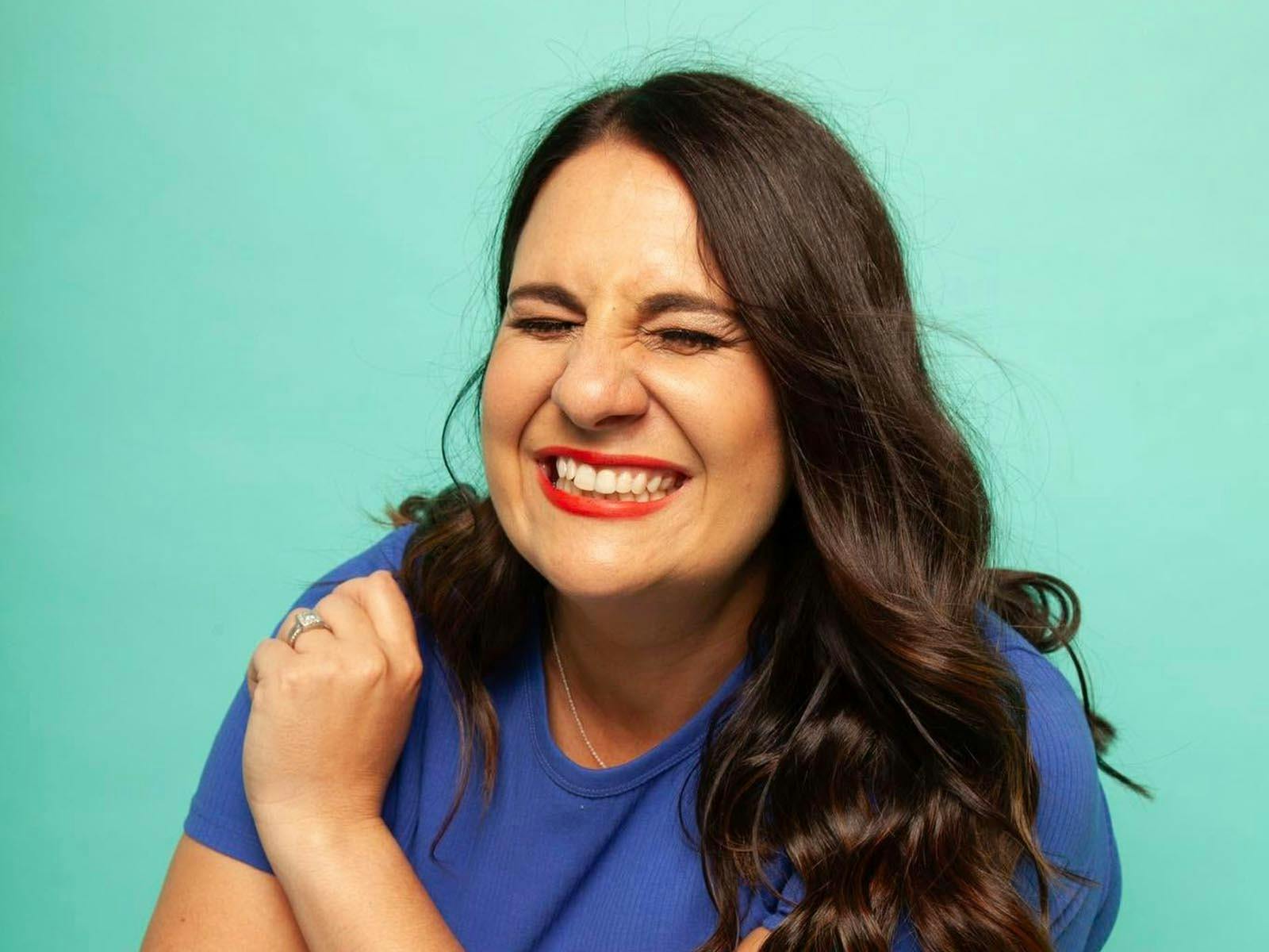 A woman with brown hair and a big smile, wearing a dark blue tshirt