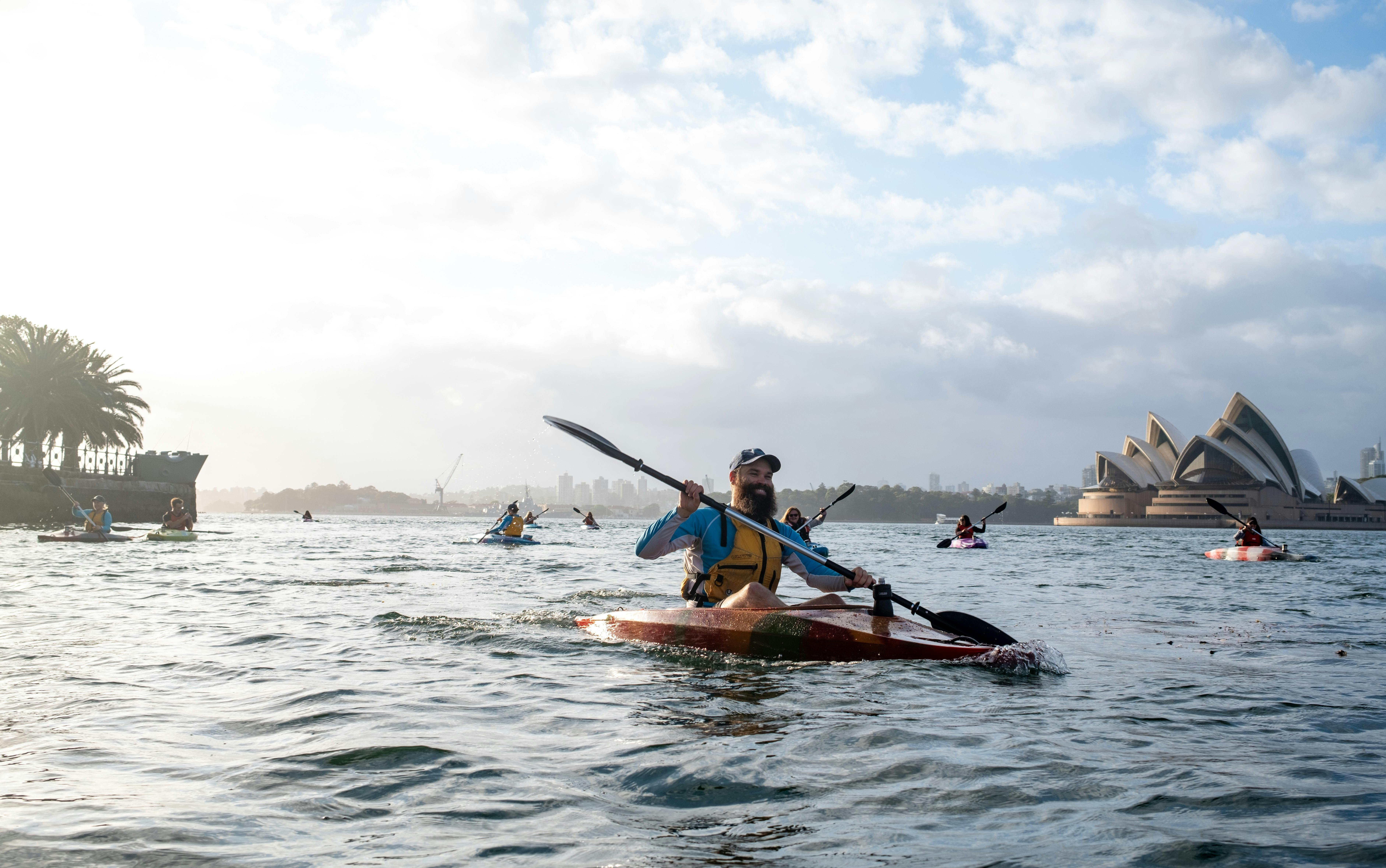 Sydney By Kayak guide showing his tour group Sydney Harbour with views of Opera House and Bridge.