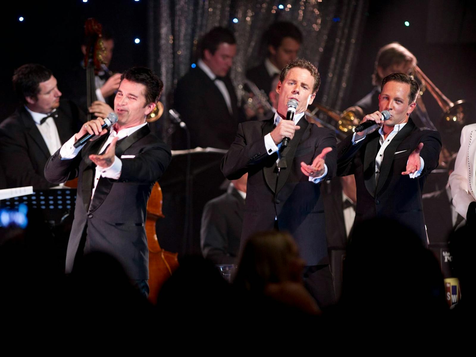 Three men in suits singing in front of a band.