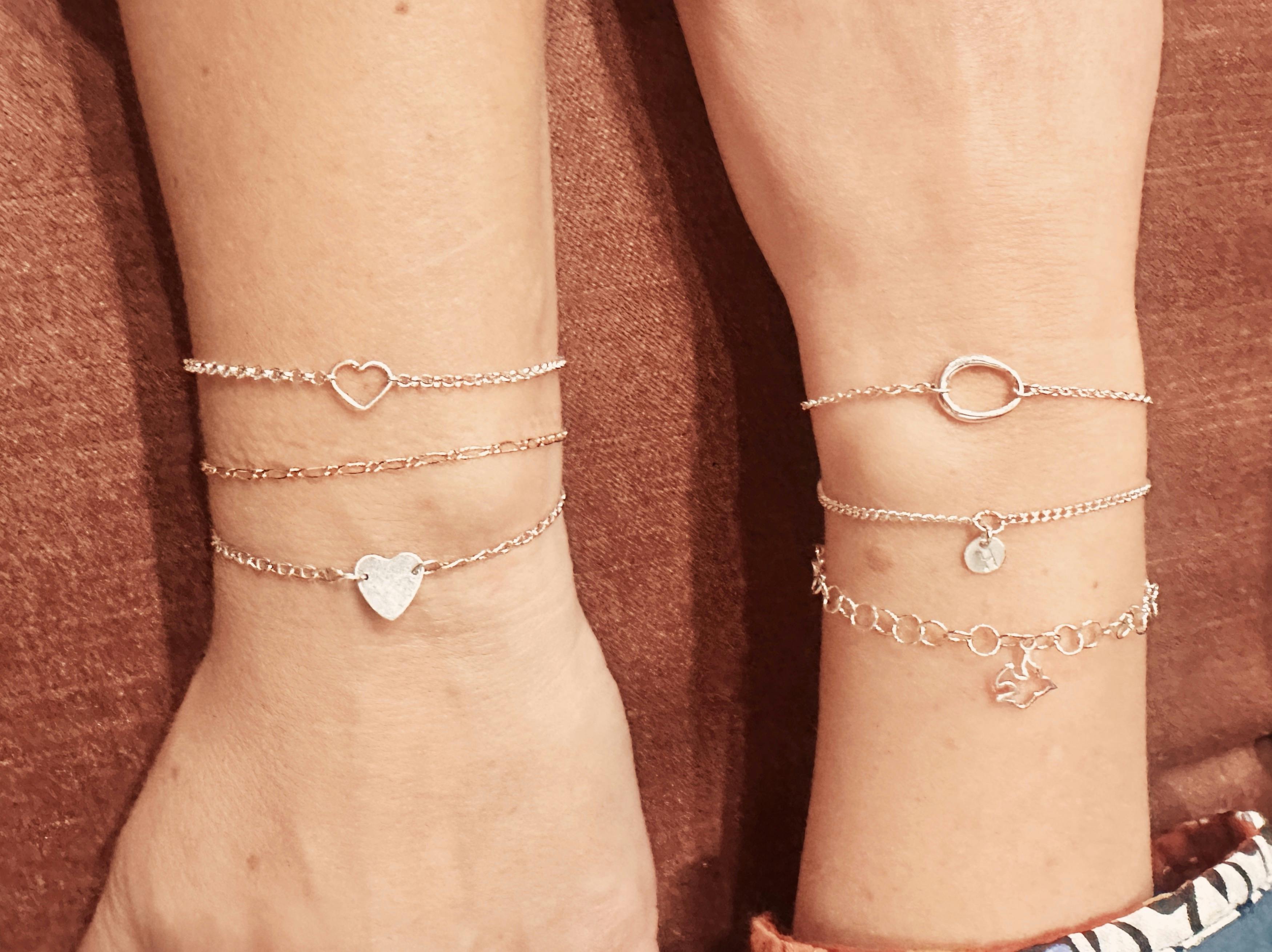 Two arms displaying a selection of sterling silver and gold permanent bracelets