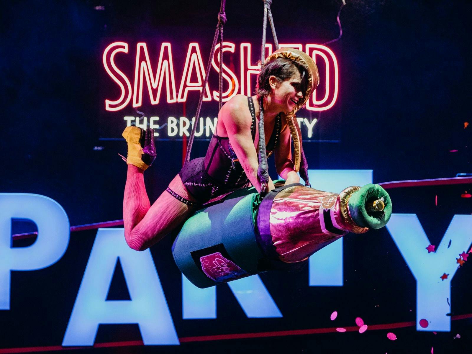 An aerial performer rides a giant champagne bottle