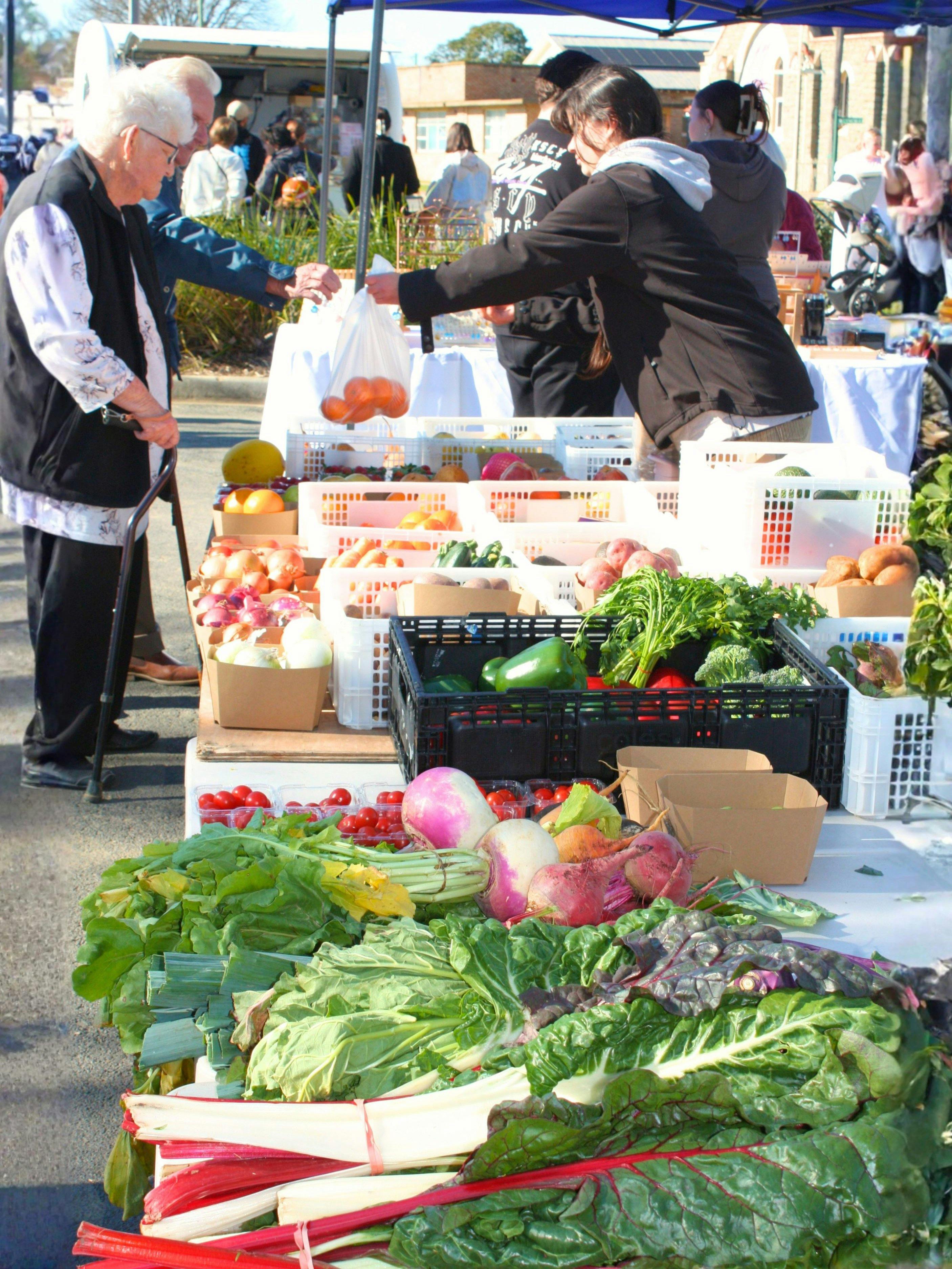 Fresh fruit and vegetables on display. An elderly couple accepting a bag of their purchased produce.