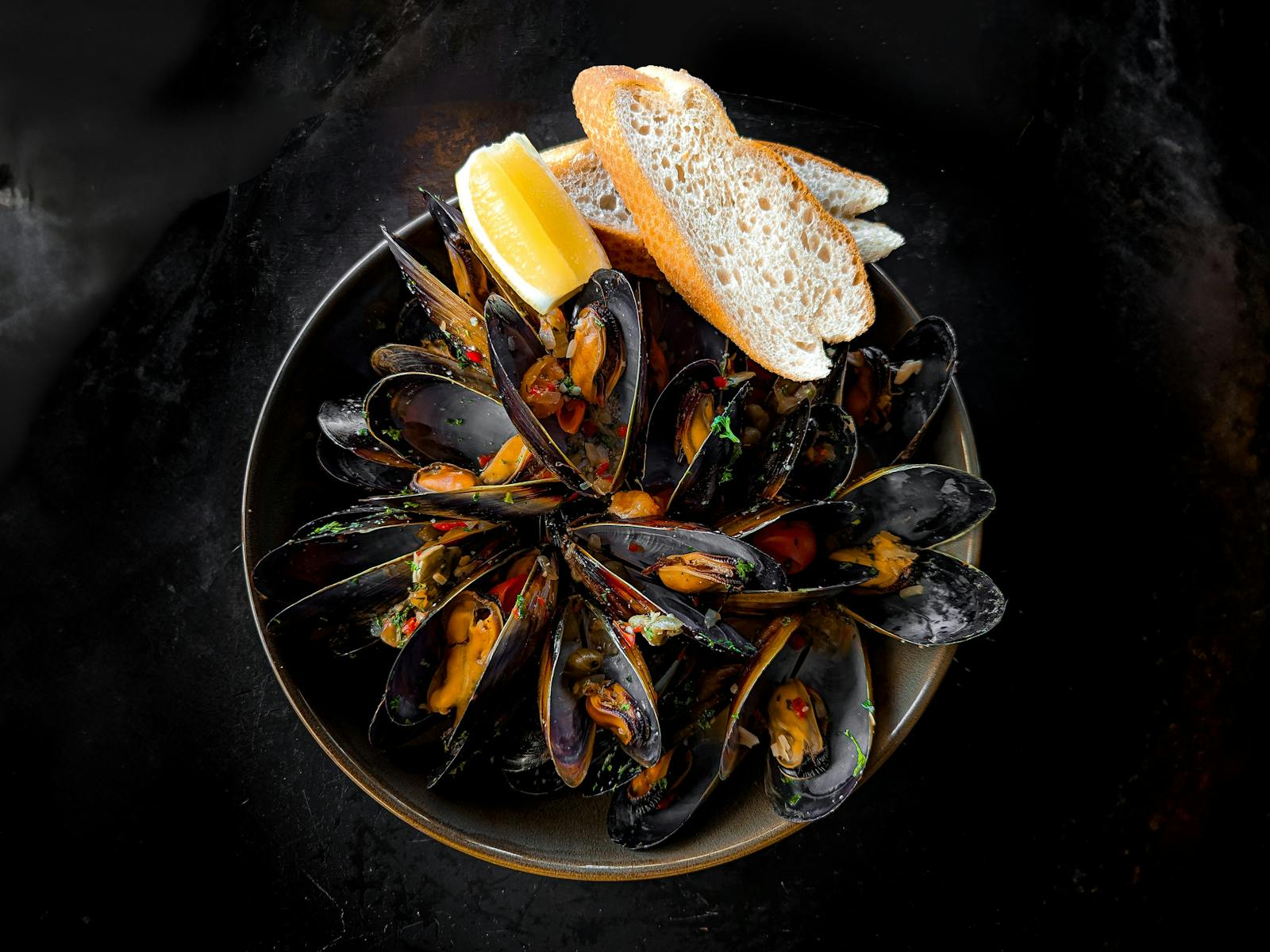 A bowl of Tasmanian Freycinet Mussels, with a  chilli sauce , two baguette slices and lemon