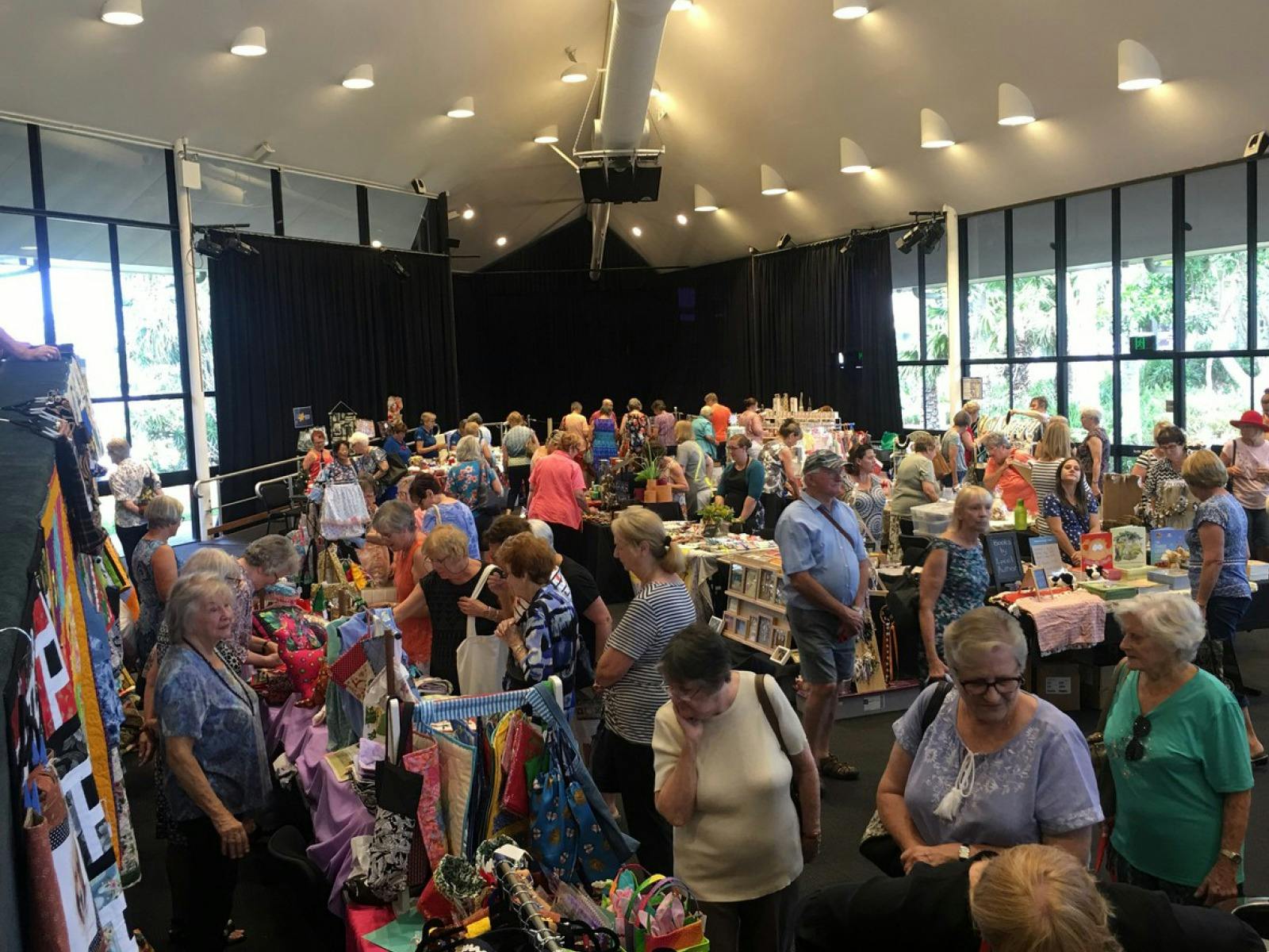 Indoor market scene with people browsing various stalls displaying crafts and goods.