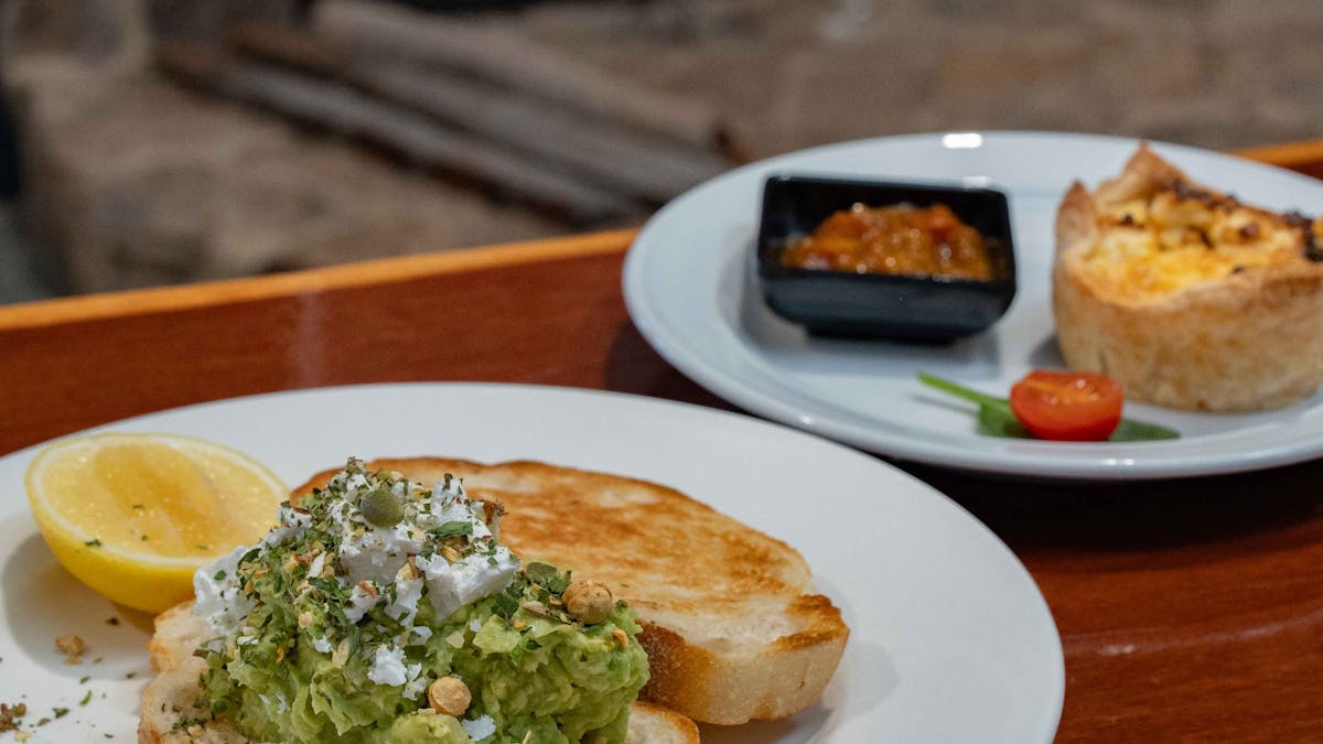 Avocado toast and a savoury quiche served on white plates in front of a warm fireplace