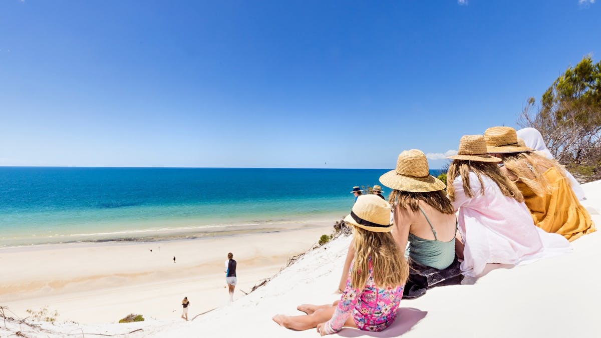 A group of children site at the top of a sand dune looking at the ocean views from K'gari