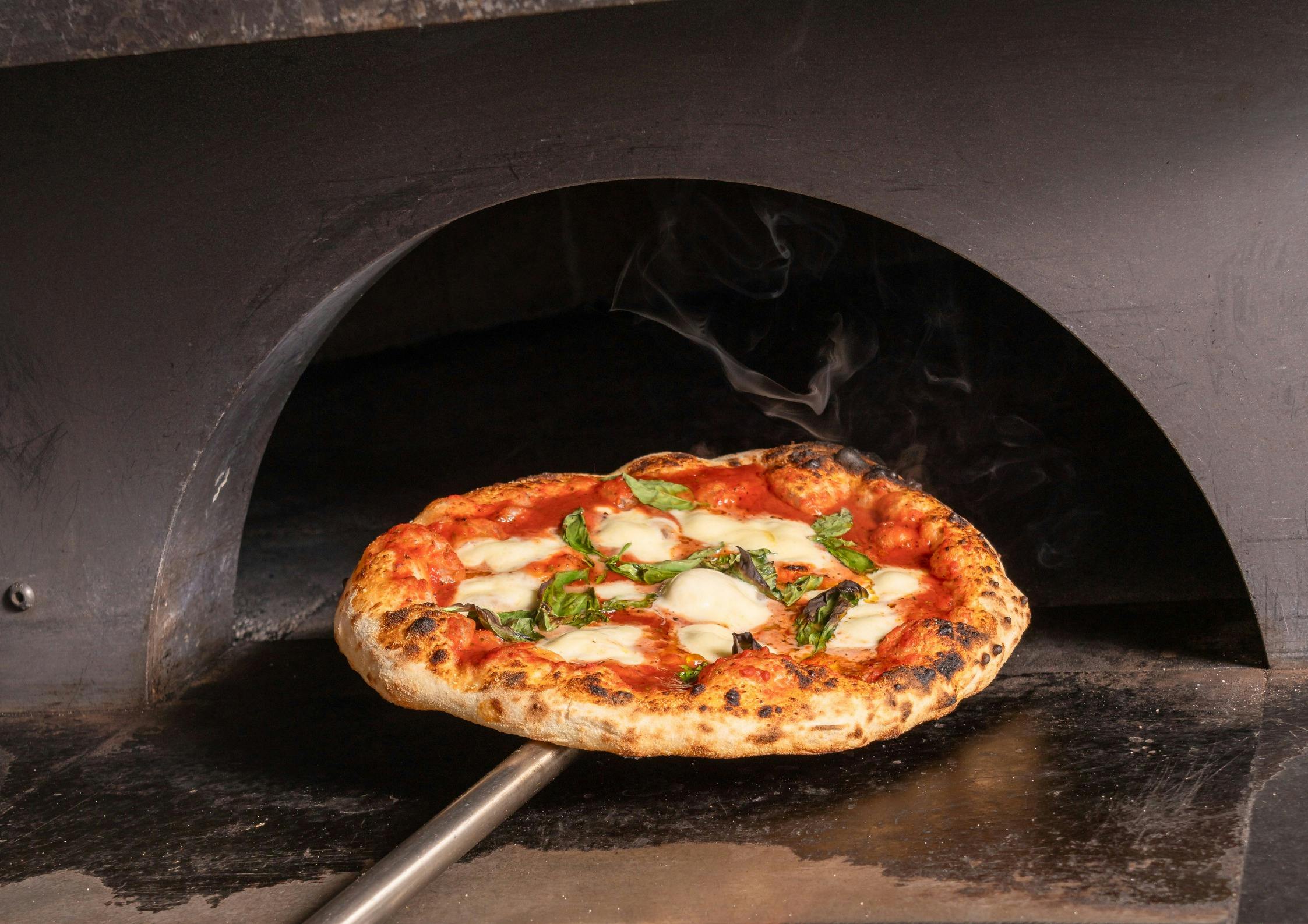a margherita pizza being pulled out of the pizza oven